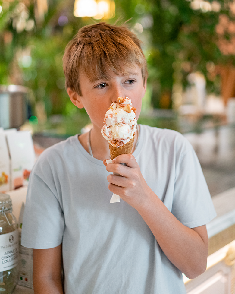 A boy with brown hair wearing a white t-shirt is holding and about to eat an ice cream cone.