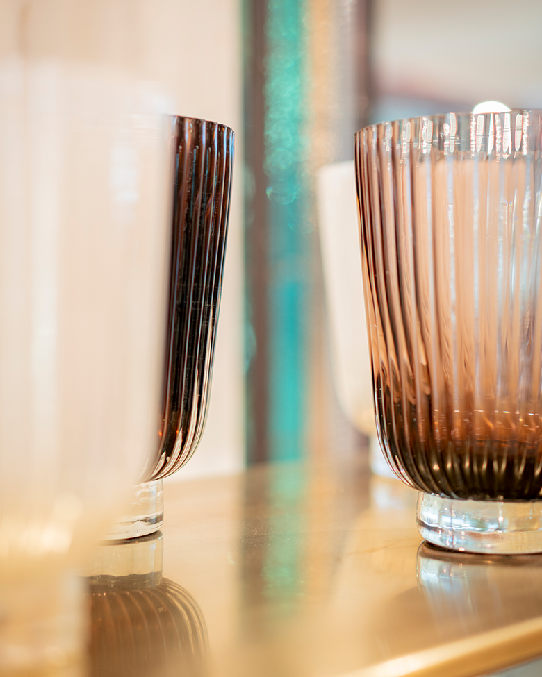Close-up of ribbed glassware on a wooden surface, with multiple glasses of varying colors and opacity.