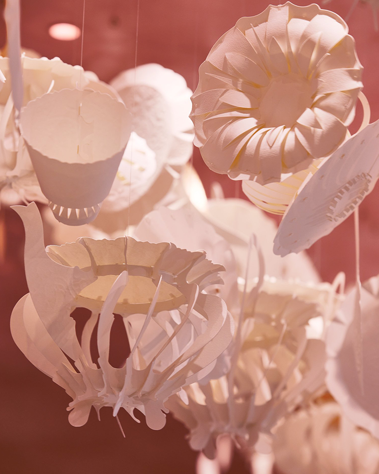 White origami-style paper lanterns and decorations hanging against a pink background.