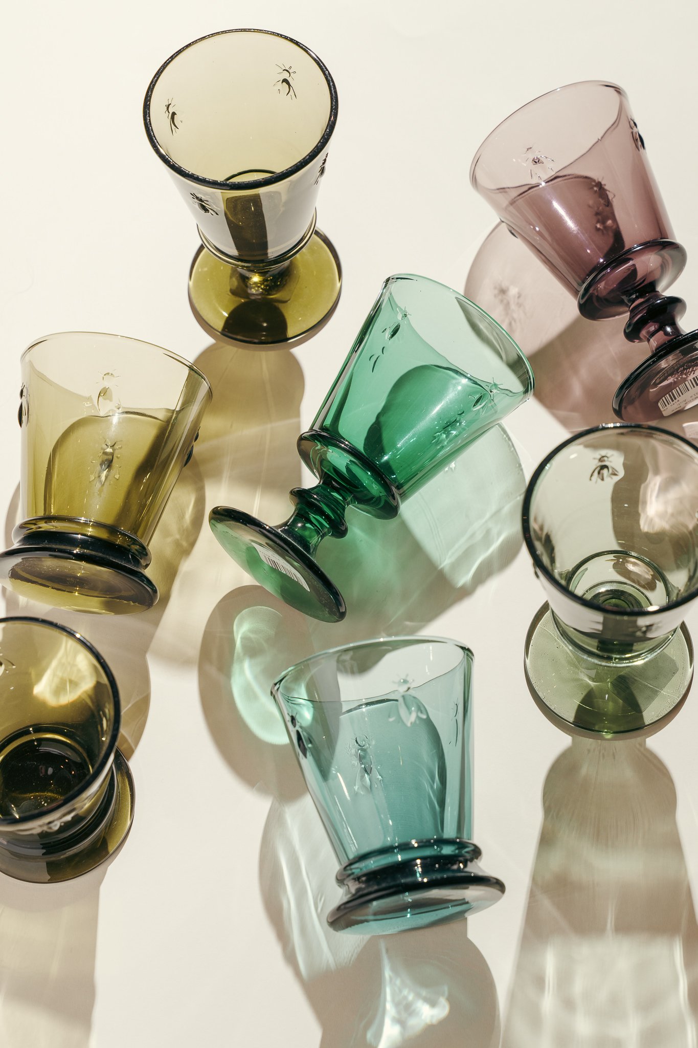 An overhead view of colorful glass cups and bowls placed on a white surface, casting shadows.