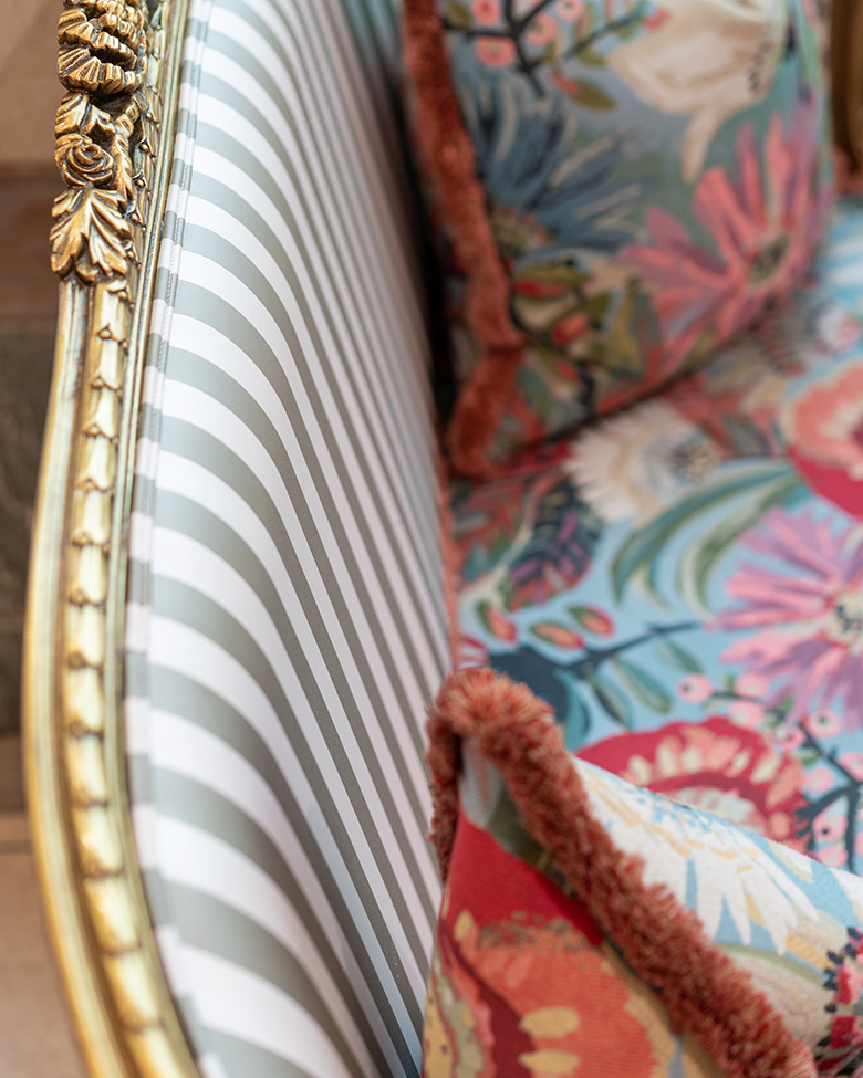 Close-up of a vintage-style sofa with a gold ornate frame, featuring striped seat cushions and floral-patterned pillows.