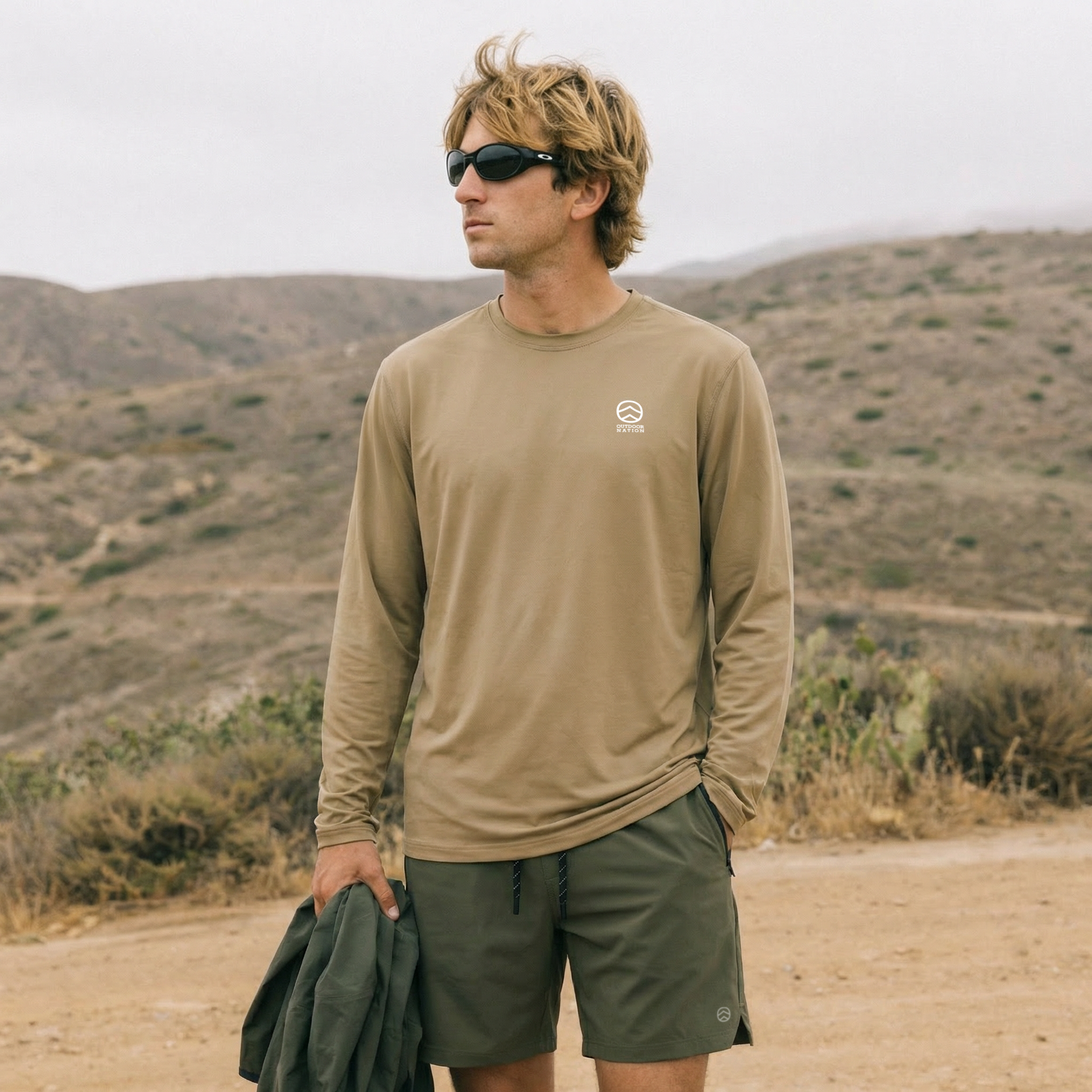 freepik_a-medium-shot-captures-a-young-man-with-tousled-blonde-hair-and-black-oakley-style-sunglasses-looking-off-to-the-side.-he-is-wearing-img2-and-img3-.-his-left-hand-is-in-his-pocket-and-he-_0001.png