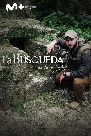 Un hombre con gorra y mochila está sentado junto a rocas en un entorno natural con vegetación densa.