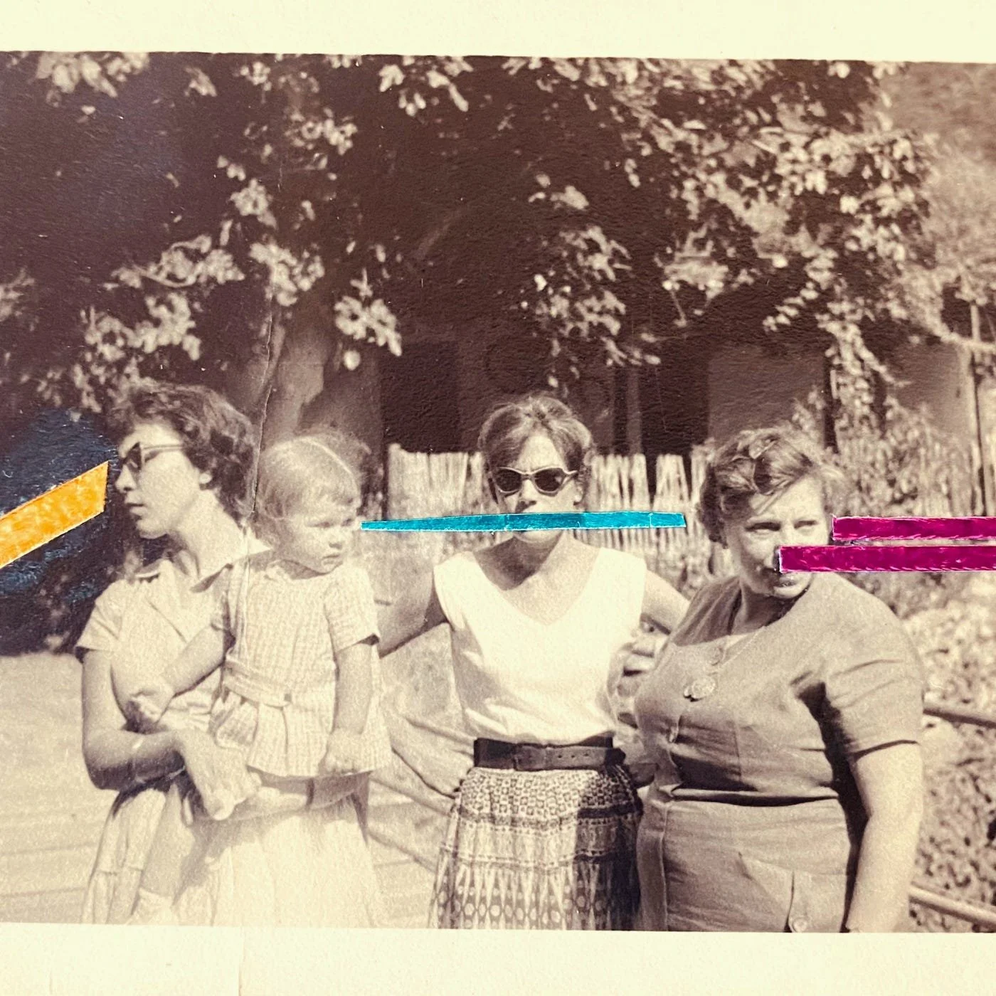 Fotografía en blanco y negro de cuatro mujeres y dos niñas con lentes de sol, en un entorno al aire libre con árboles y un cercado de madera.