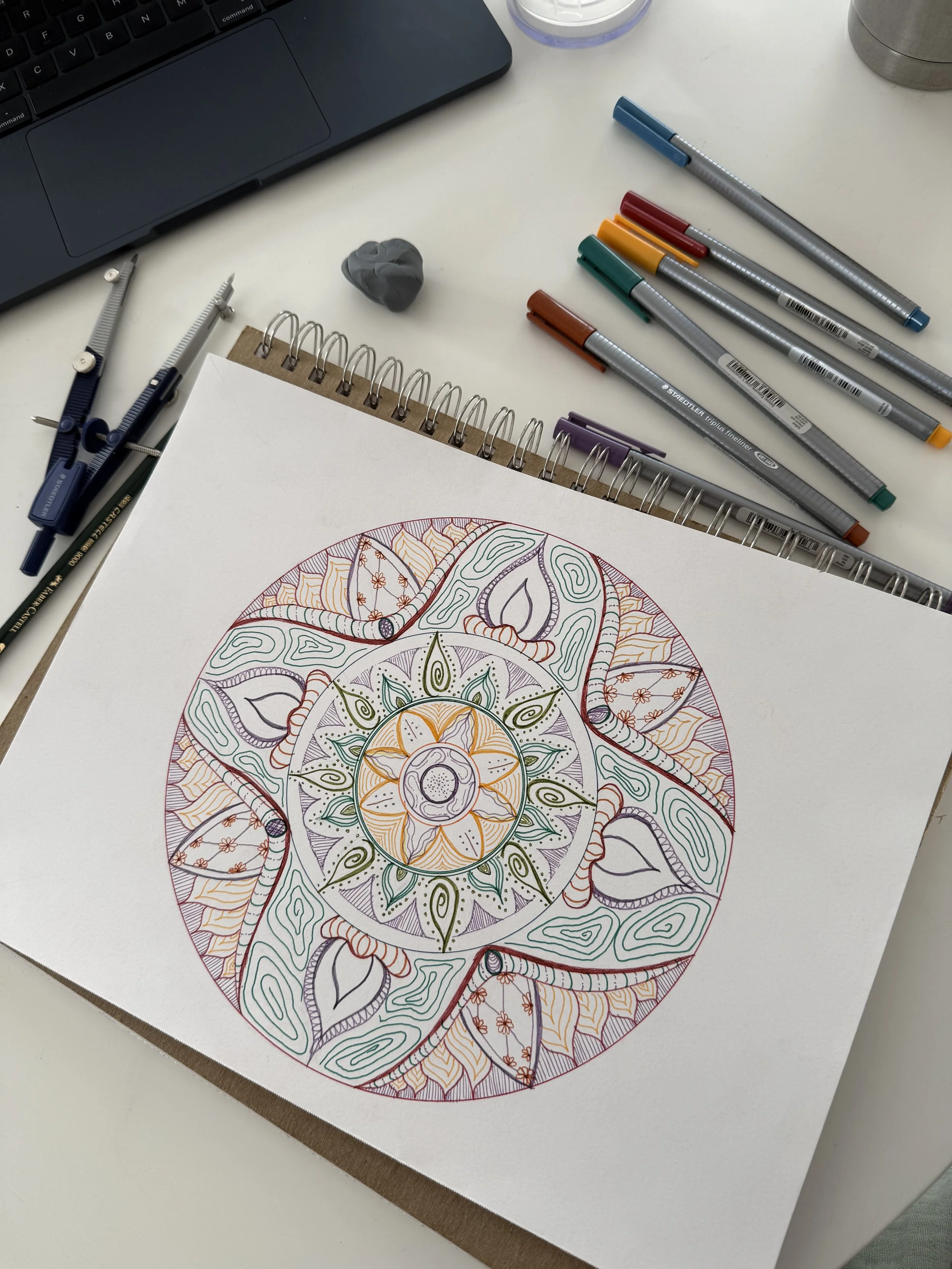 A colored mandala drawing beside pencils and drawing tools on a desk.