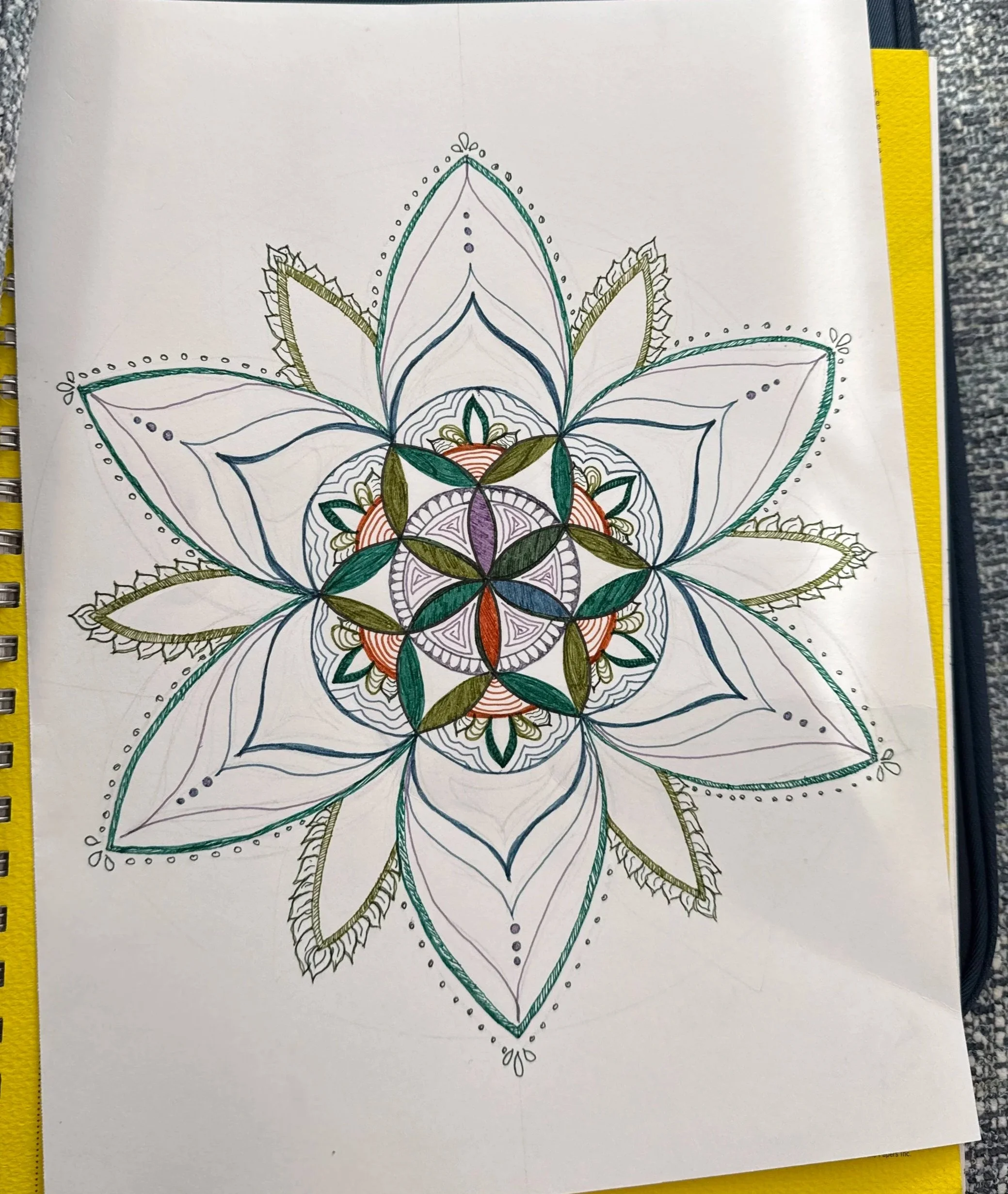 A geometric floral mandala with green, blue, and purple accents on a sketchbook page.