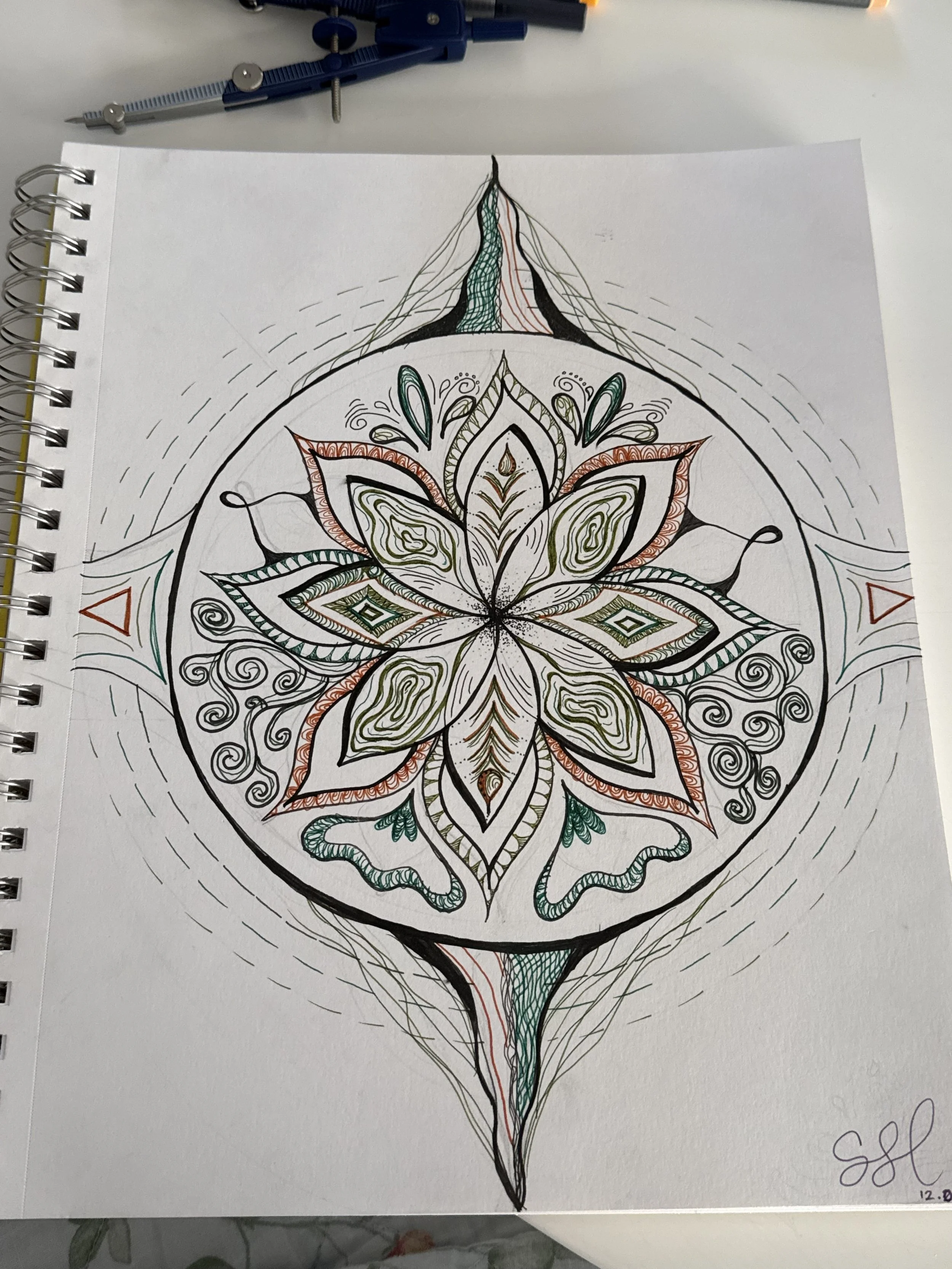 A detailed botanical mandala drawing with colored accents in a sketchbook.