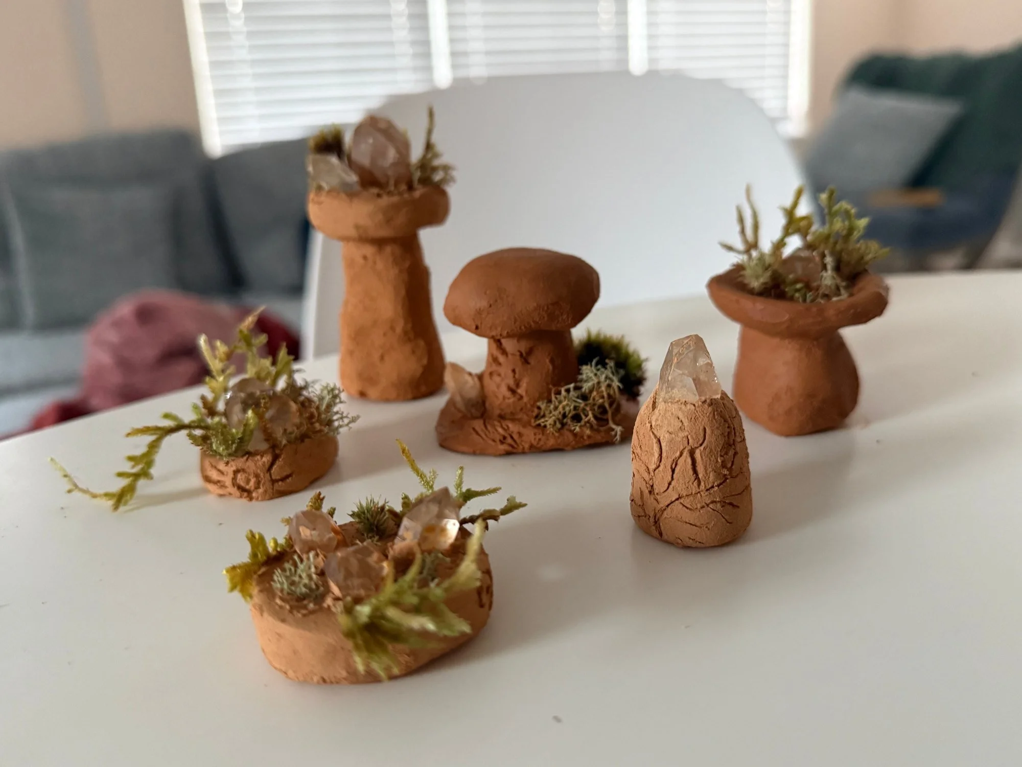 Small handmade clay vessels and mushroom forms arranged with plants on a table.