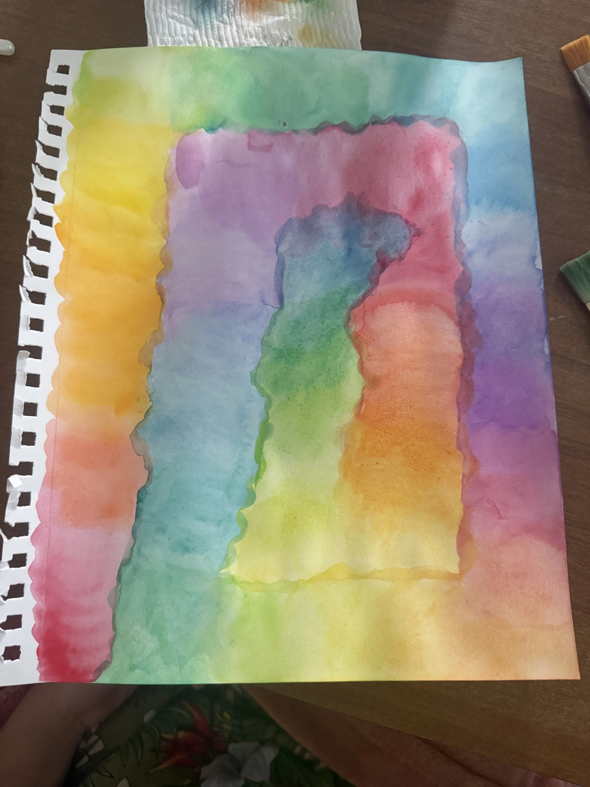 Overlapping washes of pink, blue, green, and yellow watercolor in a sketchbook.