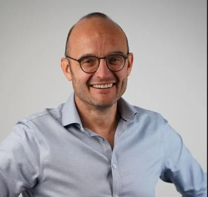Portrait of Christian Kottmann, founder of Navani & Main, smiling and wearing glasses and a light blue button-up shirt.