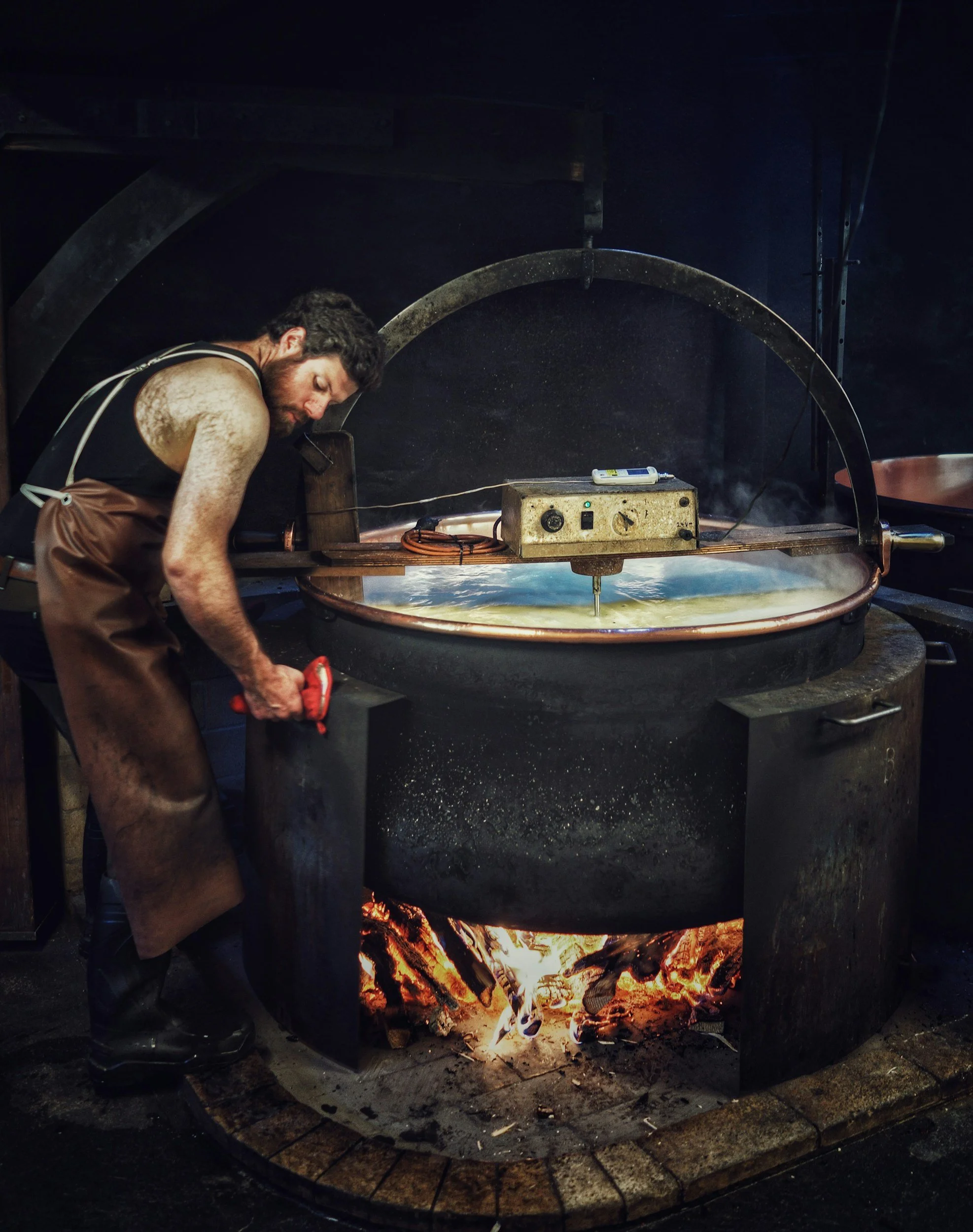 A man working near an open wood-fired oven with glowing embers and flames inside.