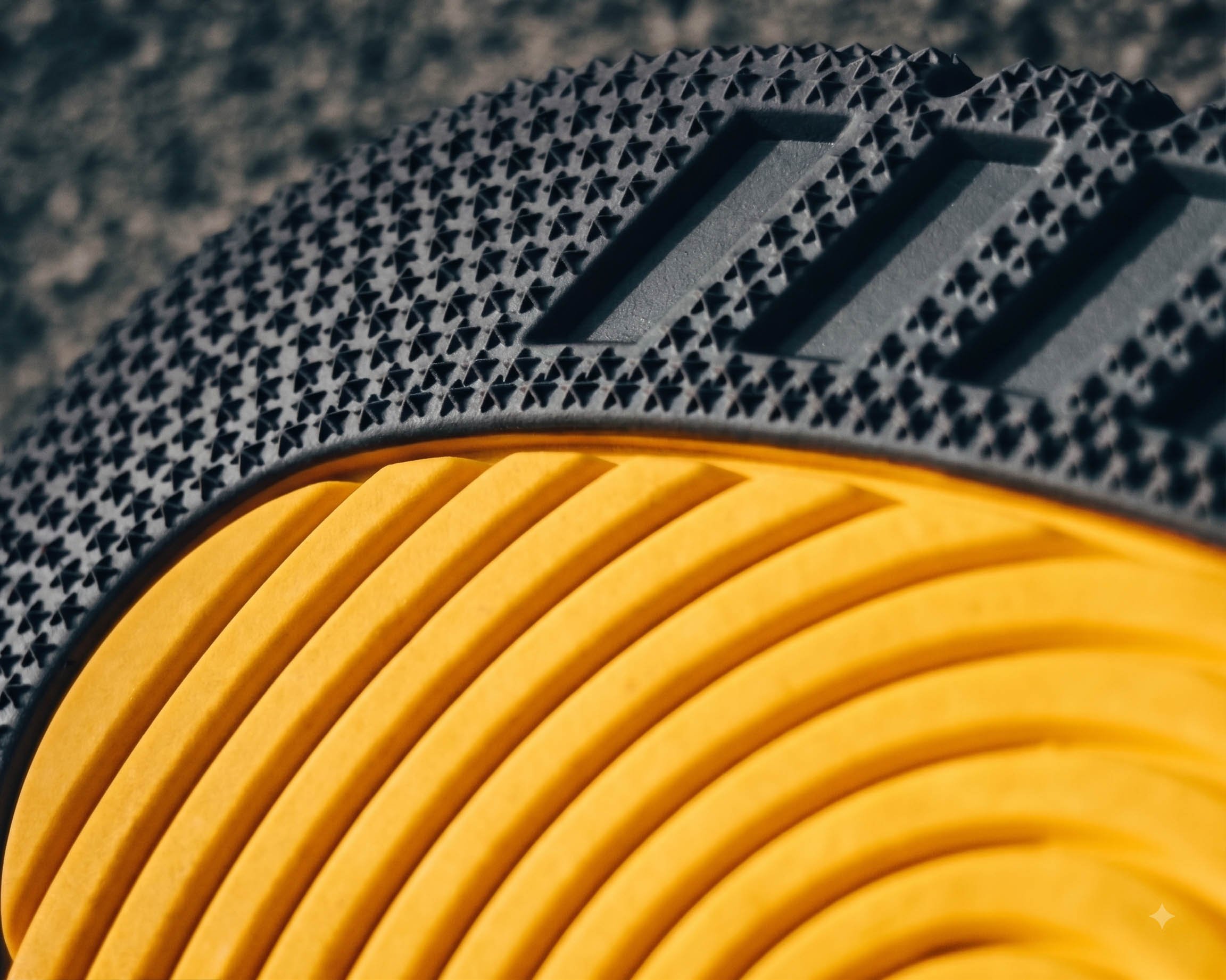 Close-up of a black and yellow sports shoe tread, showing textured rubber pattern.