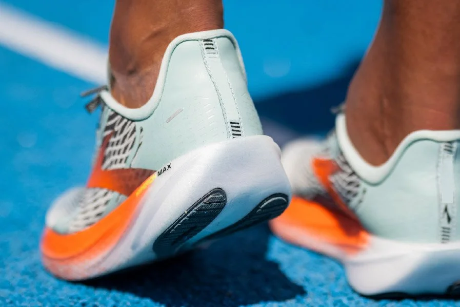 Close-up of a person's feet wearing white and orange running shoes on a blue track.