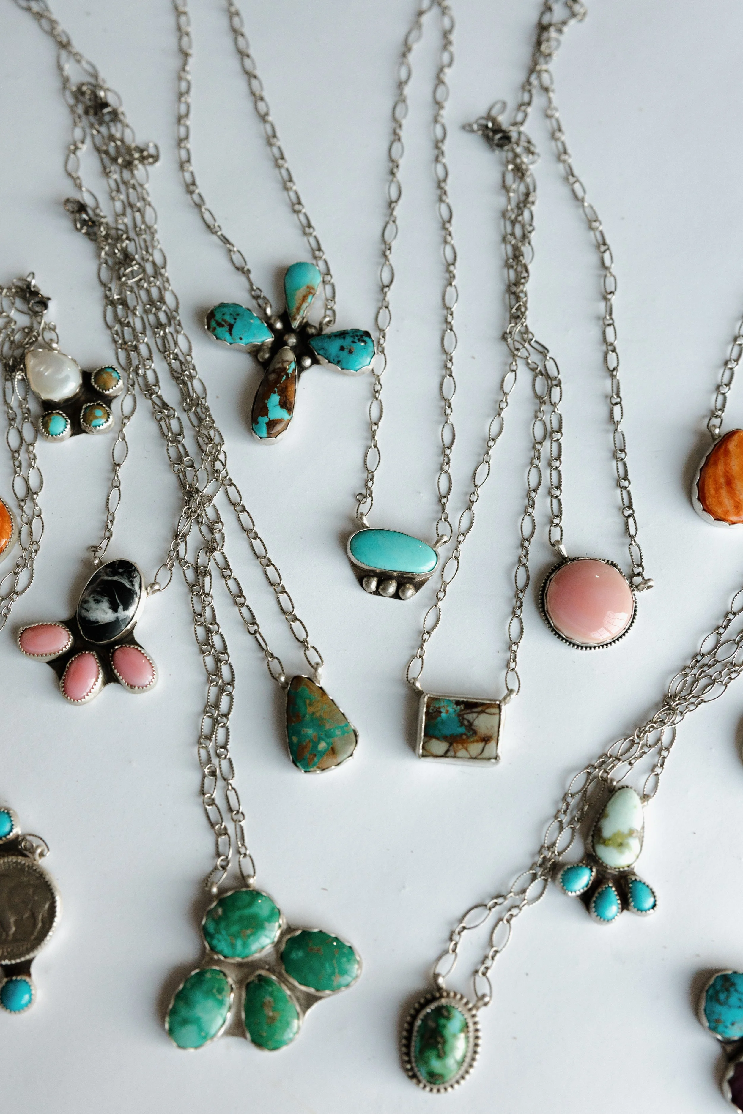 Various silver necklaces with turquoise and pink gemstone pendants laid out against a white background.