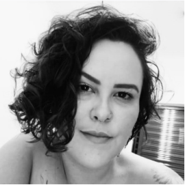 Retrato de uma mulher com cabelo cacheado e expressão neutra. Preto e branco.