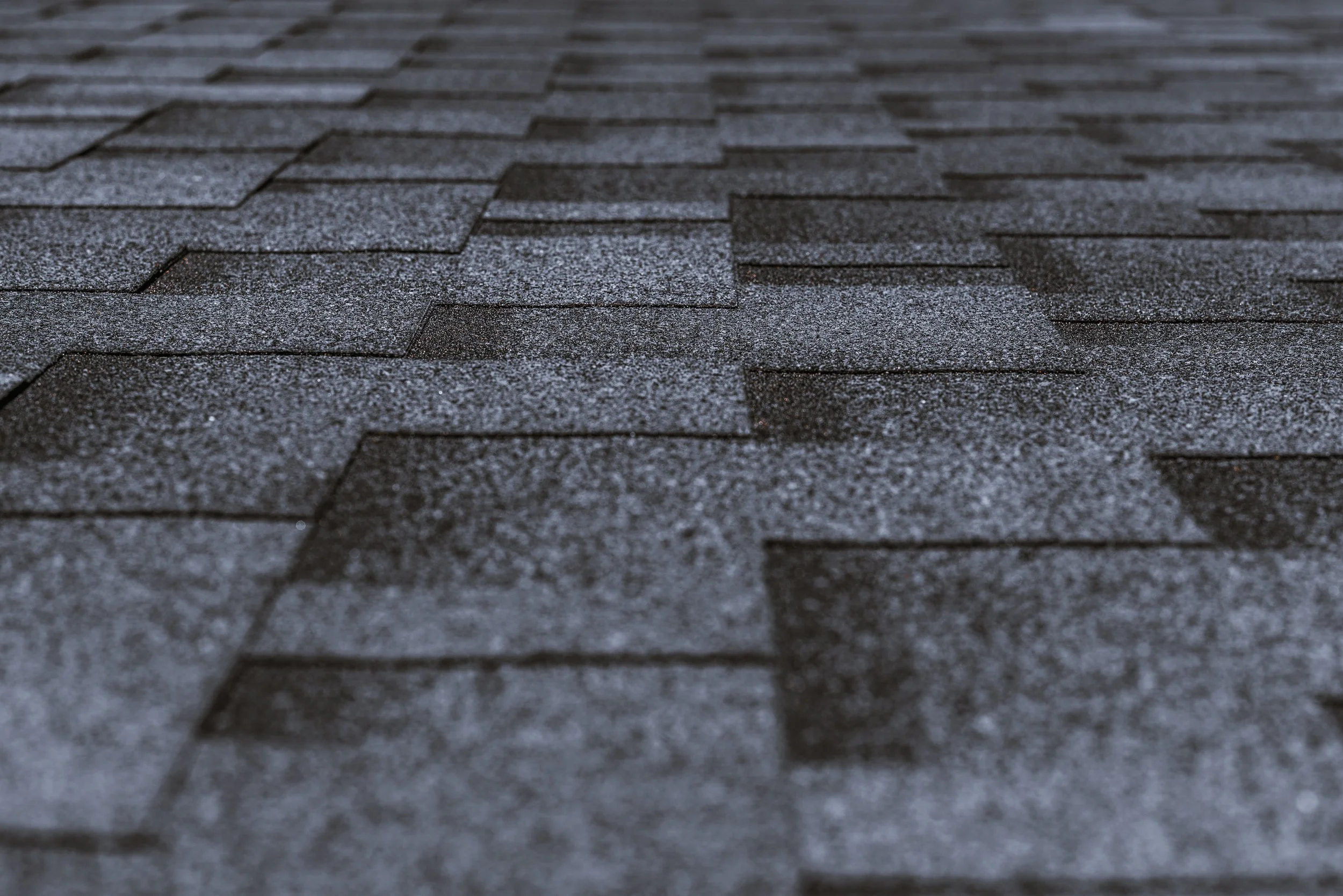 Close-up of dark gray asphalt shingles with a matte texture on a roof.