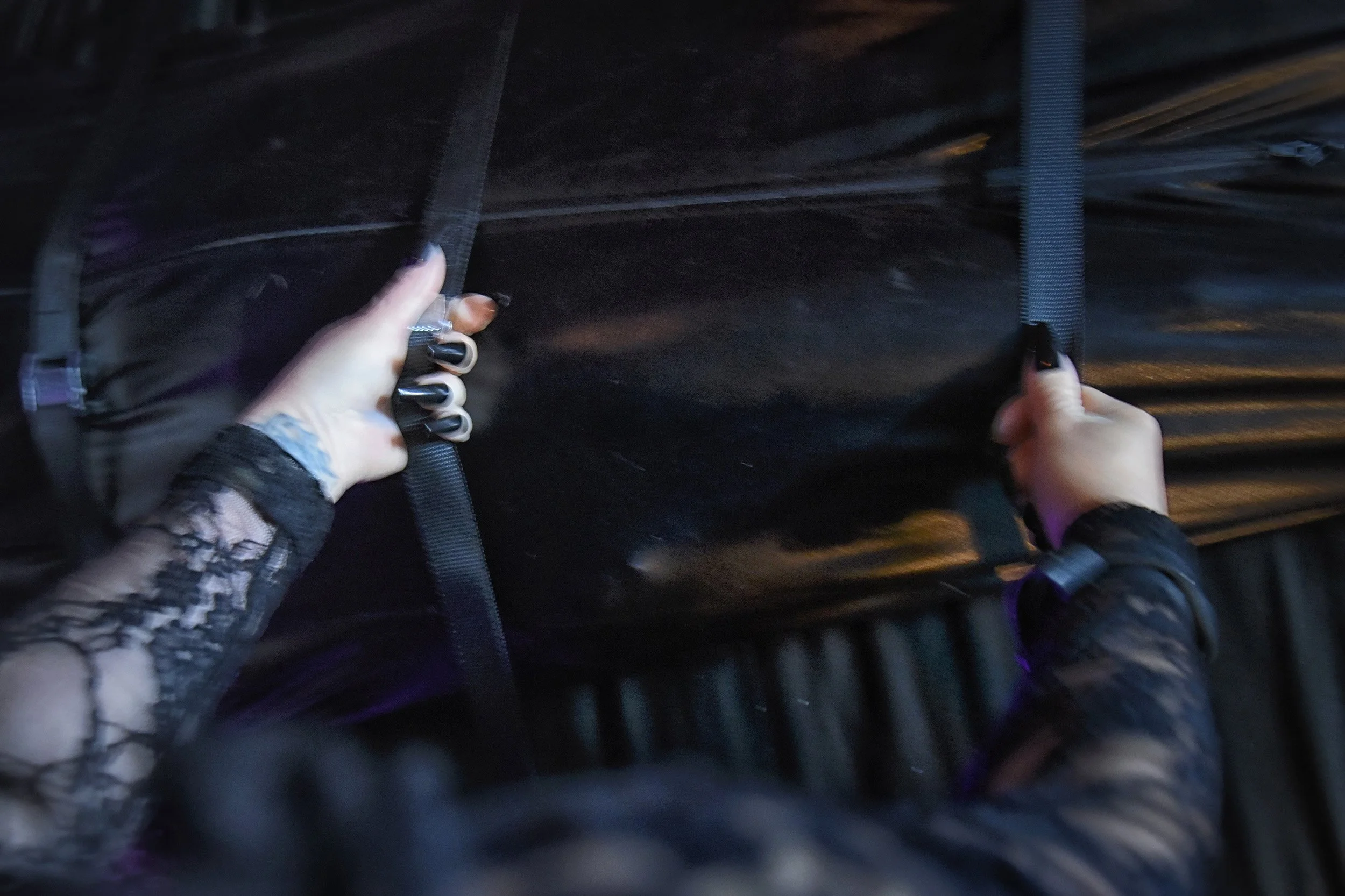 A woman holding onto black straps, on a dark bed.