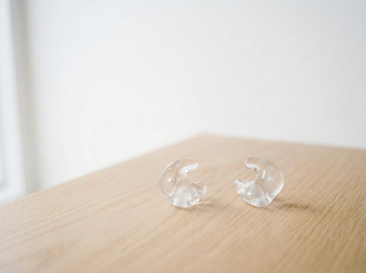 Two transparent hearing aids on a light wooden surface.