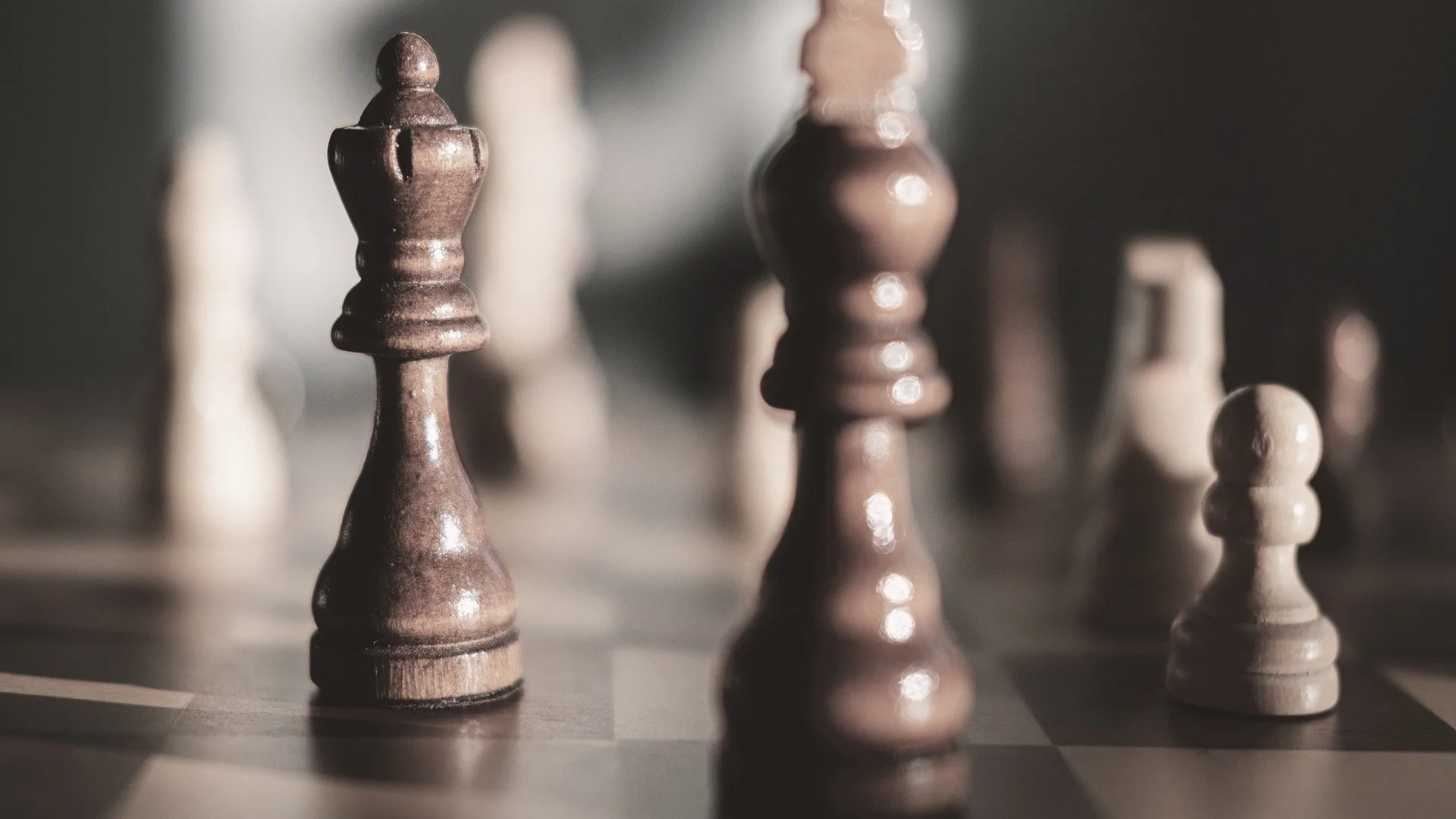 Close-up of wooden chess pieces on a chessboard, focusing on one dark rook in the foreground with other pieces blurred in the background.