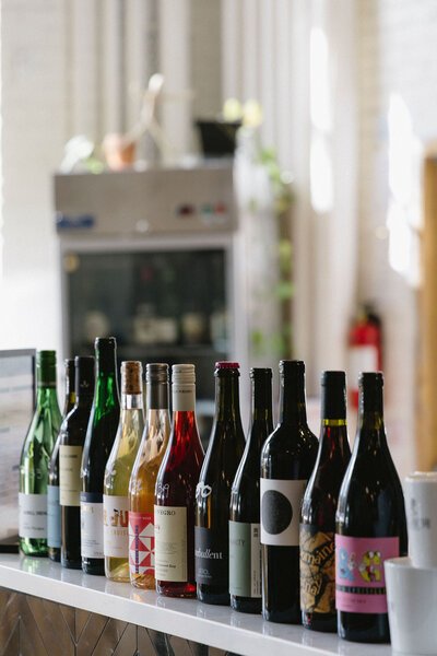 Multiple bottles of wine and sparkling drinks lined up on a kitchen counter in front of a blurry kitchen background.