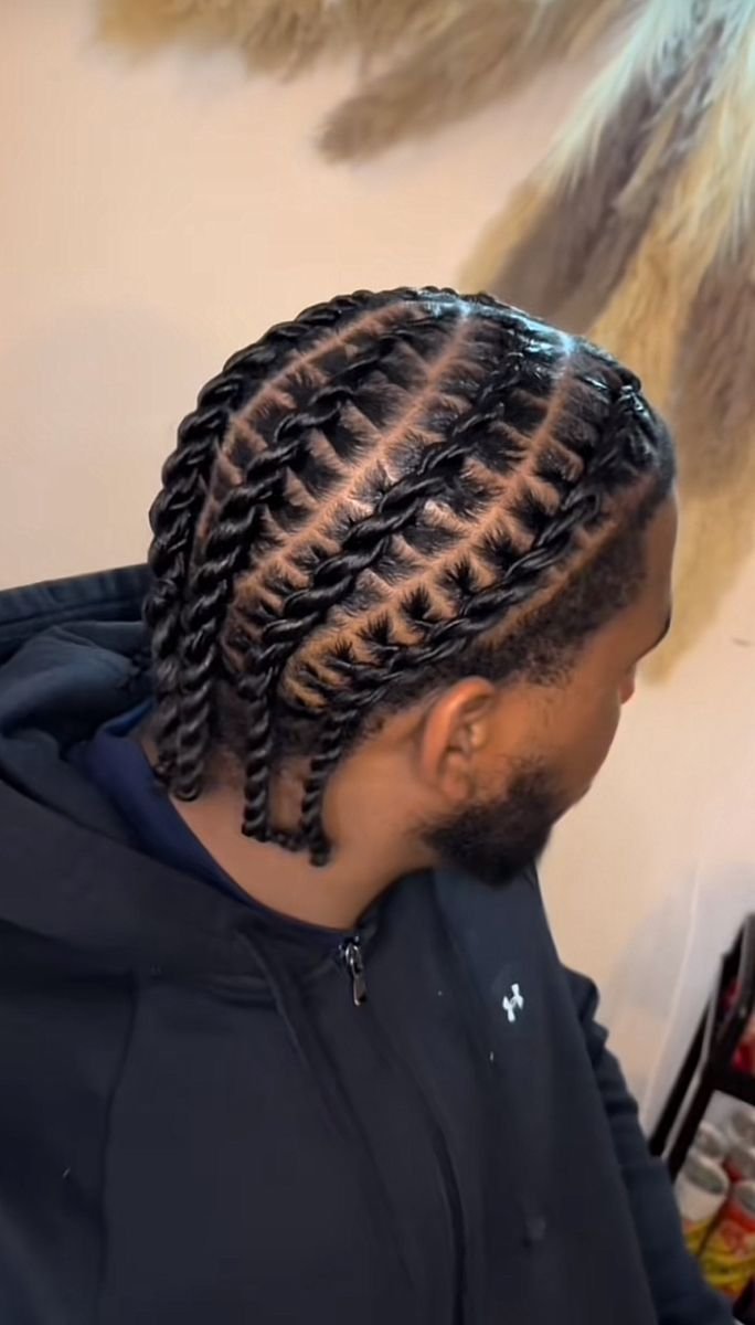 Man met strak gevlochten haar met centrale scheiding en een baard, gekleed in een zwart jasje.