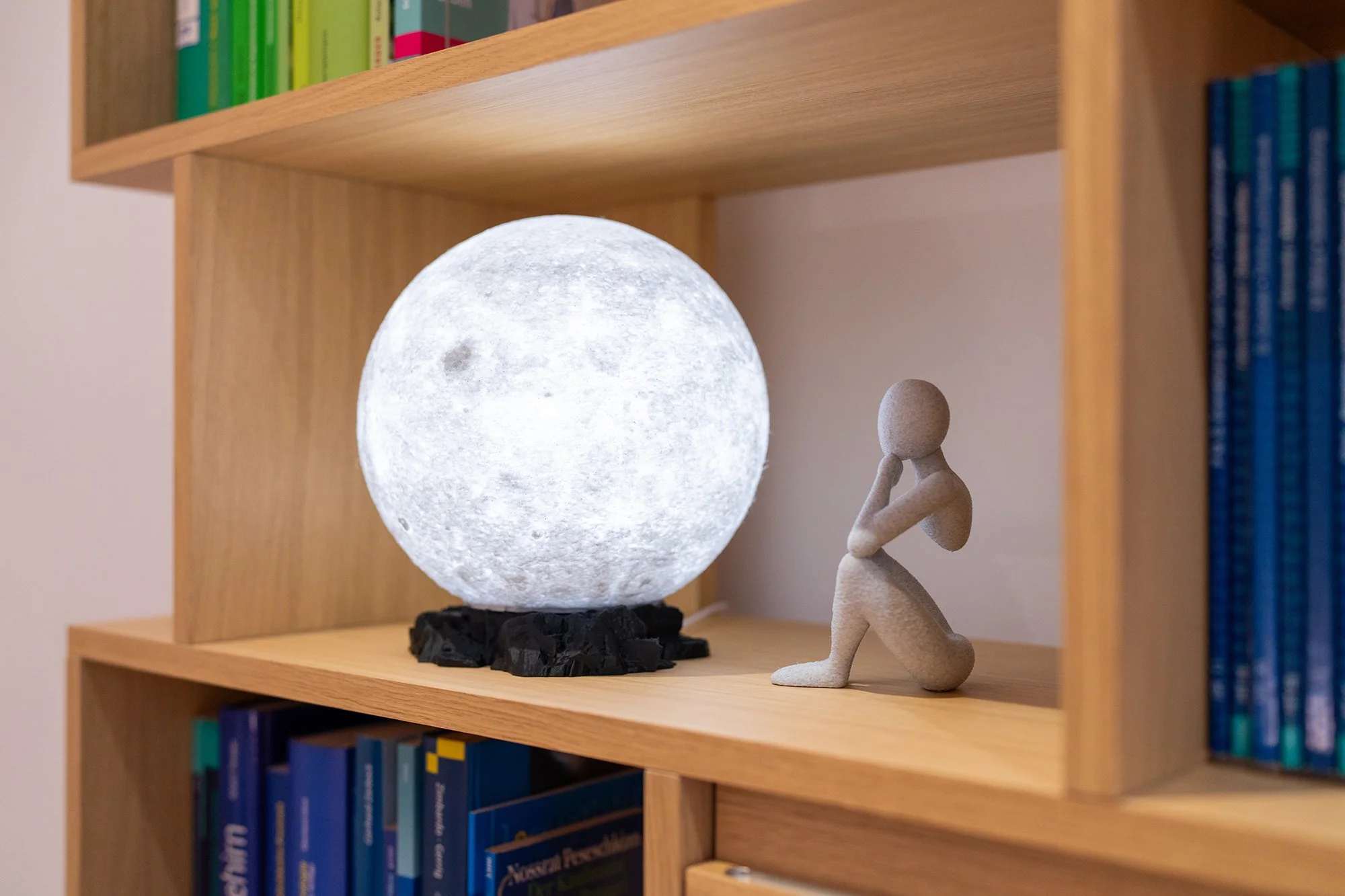 In einem Bücherregal in der Psychotherapiepraxis Sandra Hahn steht neben Fachliteratur eine leuchtende Mondlampe und eine Deko-Figur eines sitzenden Menschen. (Foto: Tobias Härtel)