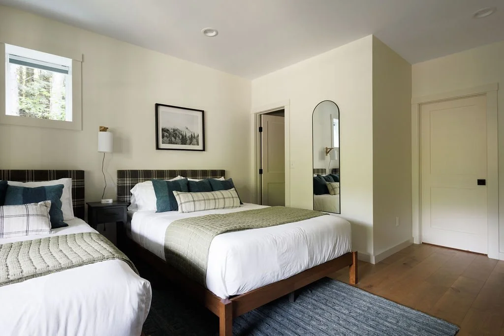 A bedroom with two beds, a window, a framed picture, a mirror, a door, and minimalist decor.