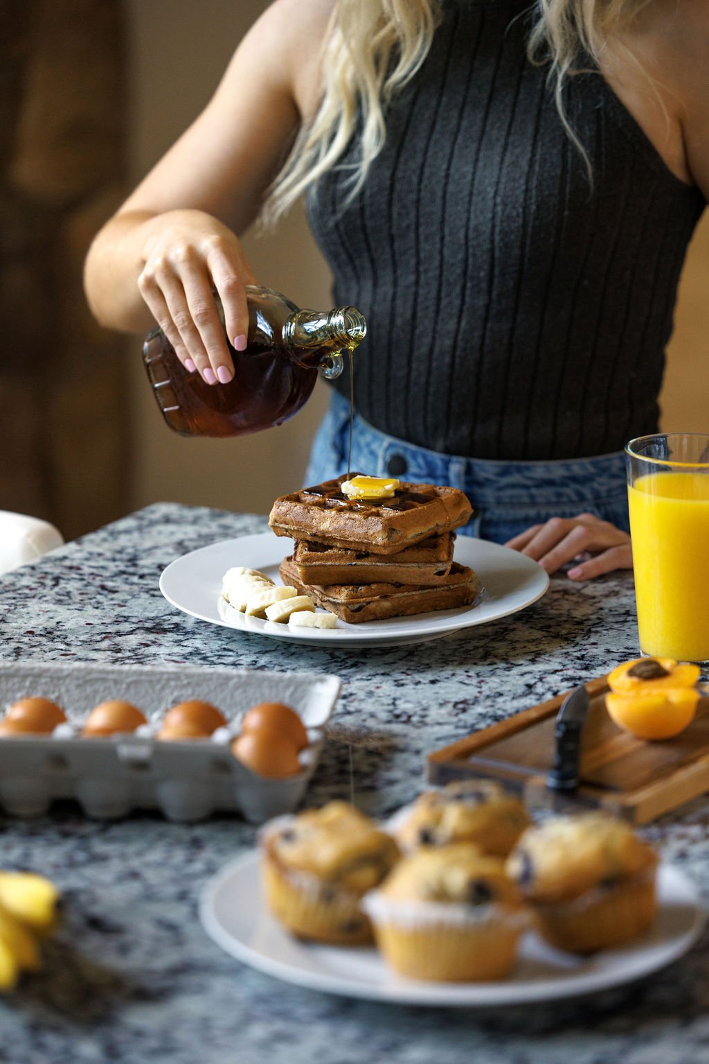 Woman pouring syrup over waffles on a plate in breakfast setting.