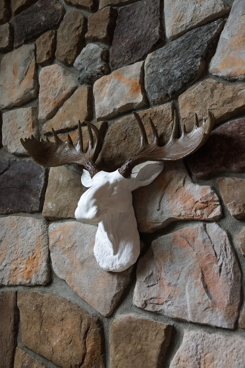 A decorative mounted white deer head with large dark brown antlers on a textured stone wall.
