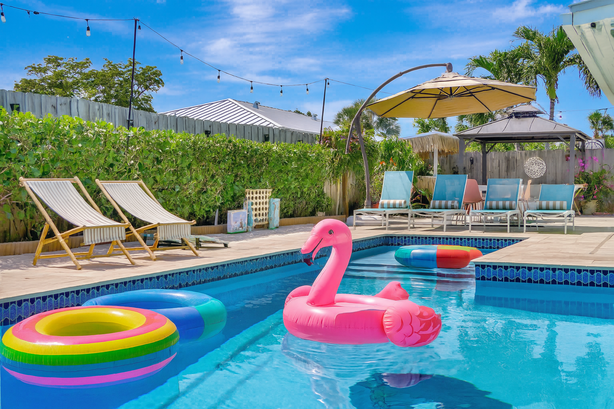 Backyard swimming pool with colorful pool floats, lounge chairs, an umbrella, and outdoor seating area under a string of lights.