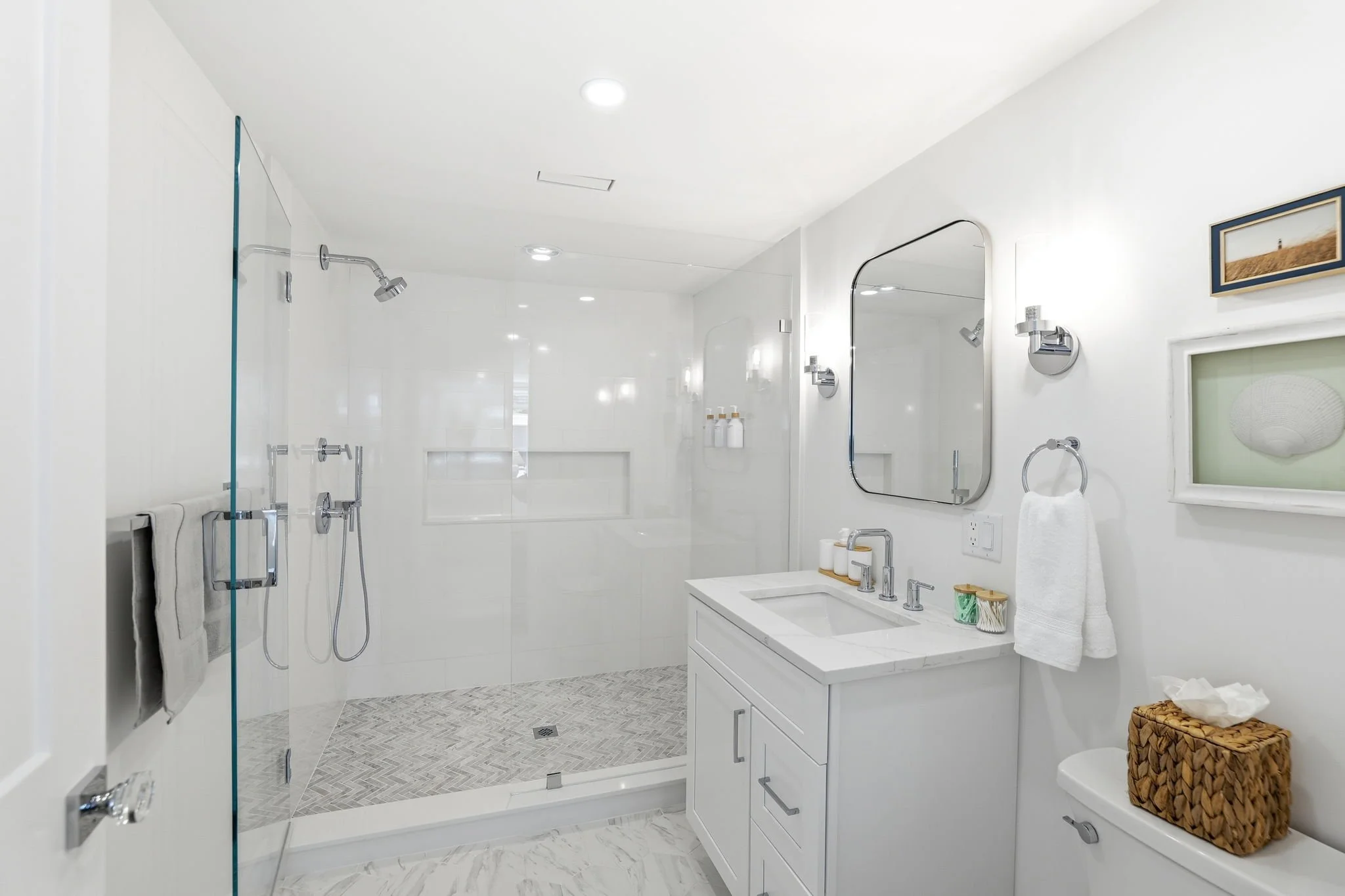 Clean, modern bathroom with white walls, a glass shower enclosure, and a white vanity with a sink, mirror, and wall-mounted lighting.