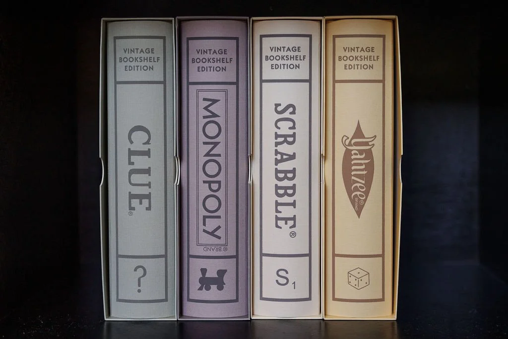 Four vintage bookshelf edition board game boxes titled Club, Monopol, Scrabble, and Yahtzee, arranged upright on a dark surface.