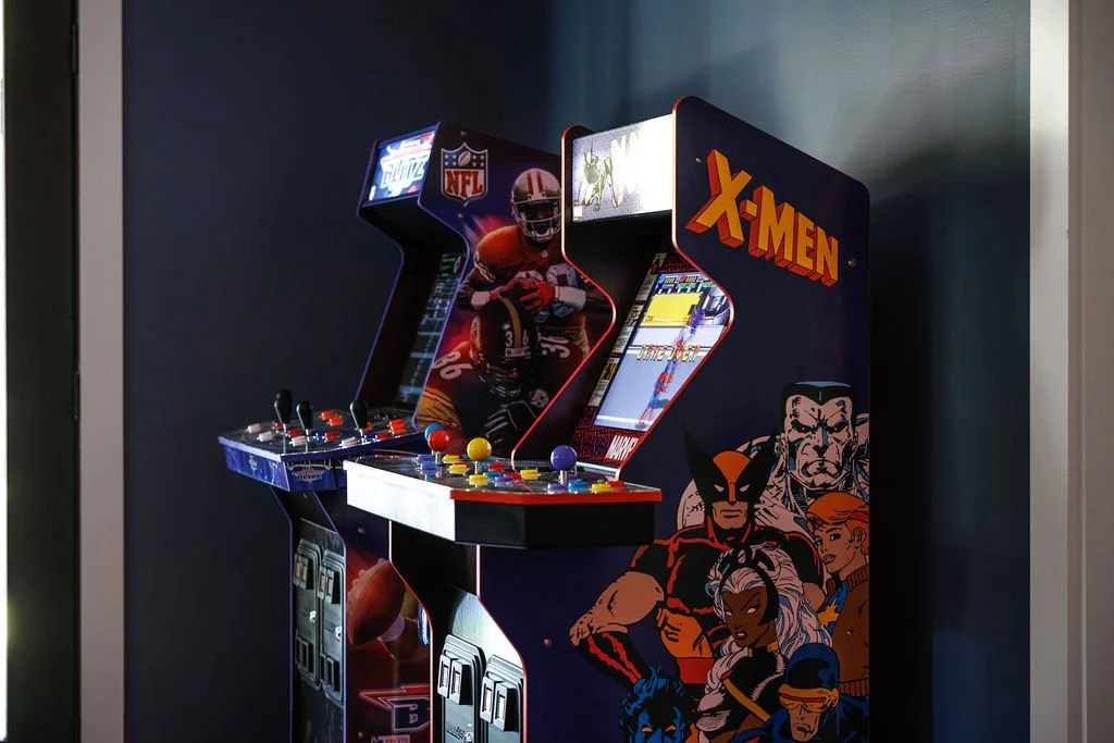 An arcade machine featuring characters from the X-Men comic series, with a control panel that has colorful joystick and buttons, set against a dark background.