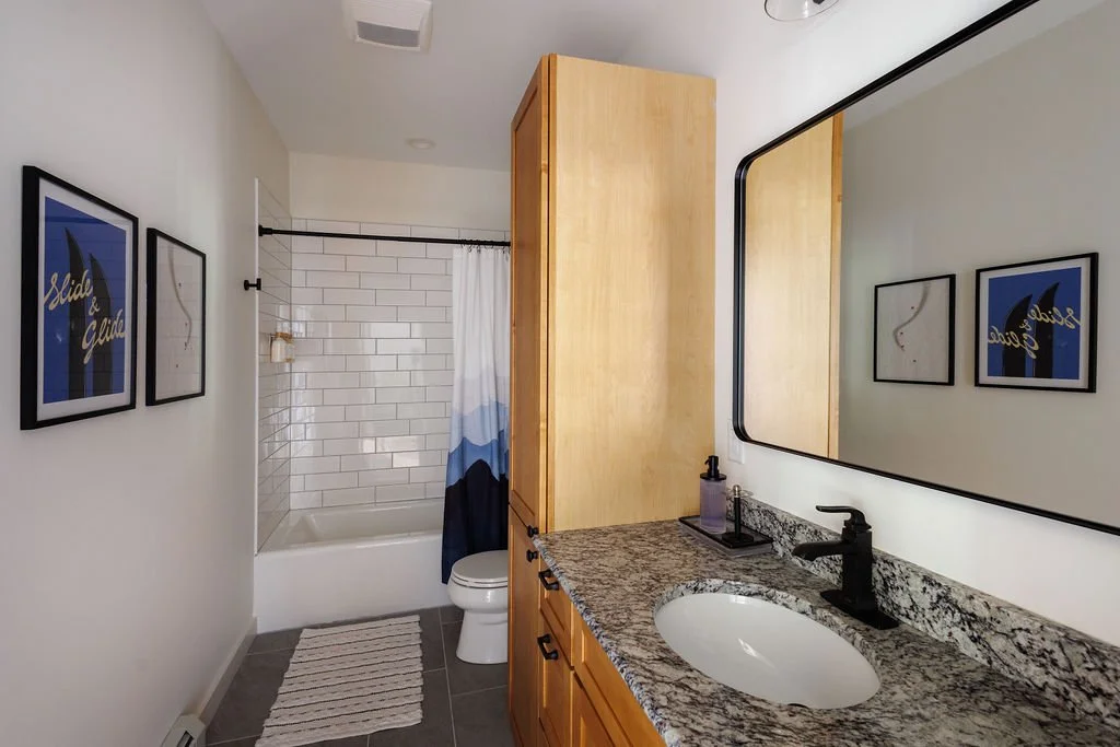 Bathroom with a single sink vanity, large mirror, framed art on the wall, and a bathtub with a shower curtain.