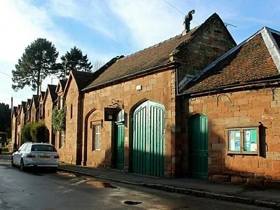 A street view of old stone buildings with green doors and a man standing on the roof, under a blue sky.