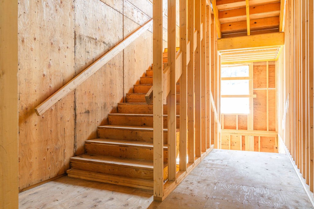 Interior view of a building under construction showing wooden stairs, framing, and a window.