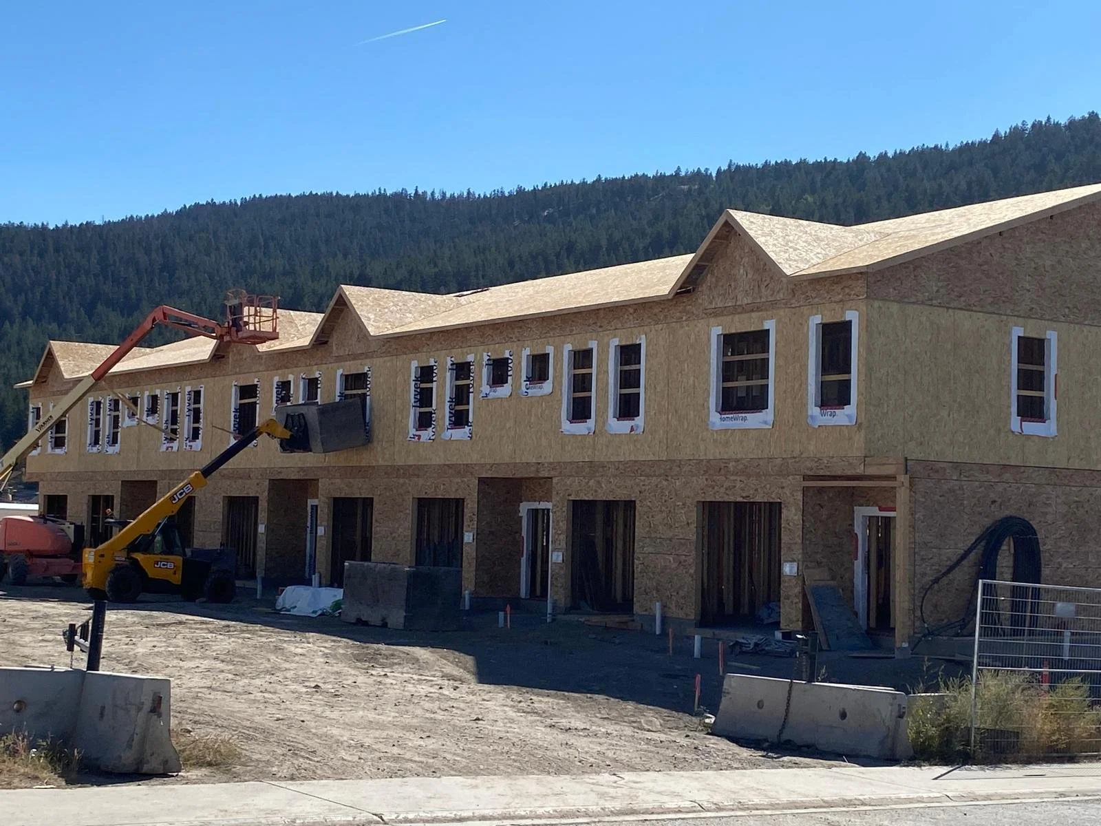 Under construction building with wooden framing, construction equipment, and a scenic mountain background.