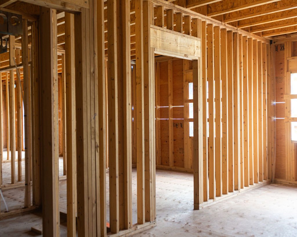Interior view of a building under construction, showing wooden framing and studs.