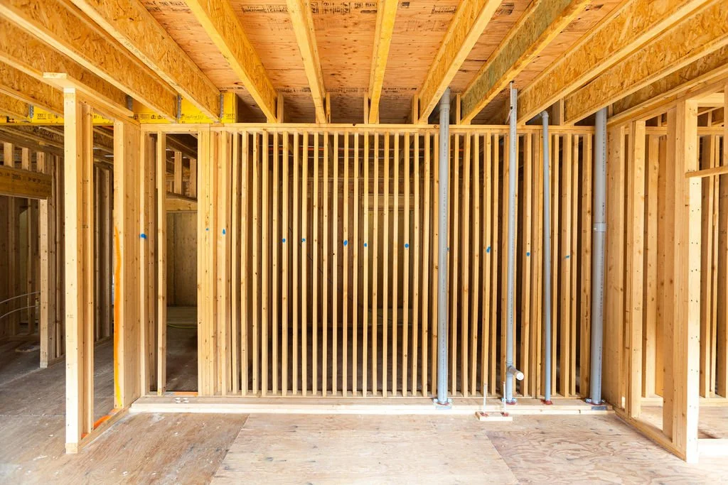 Interior view of a building under construction with wooden framing and vertical metal pipes.