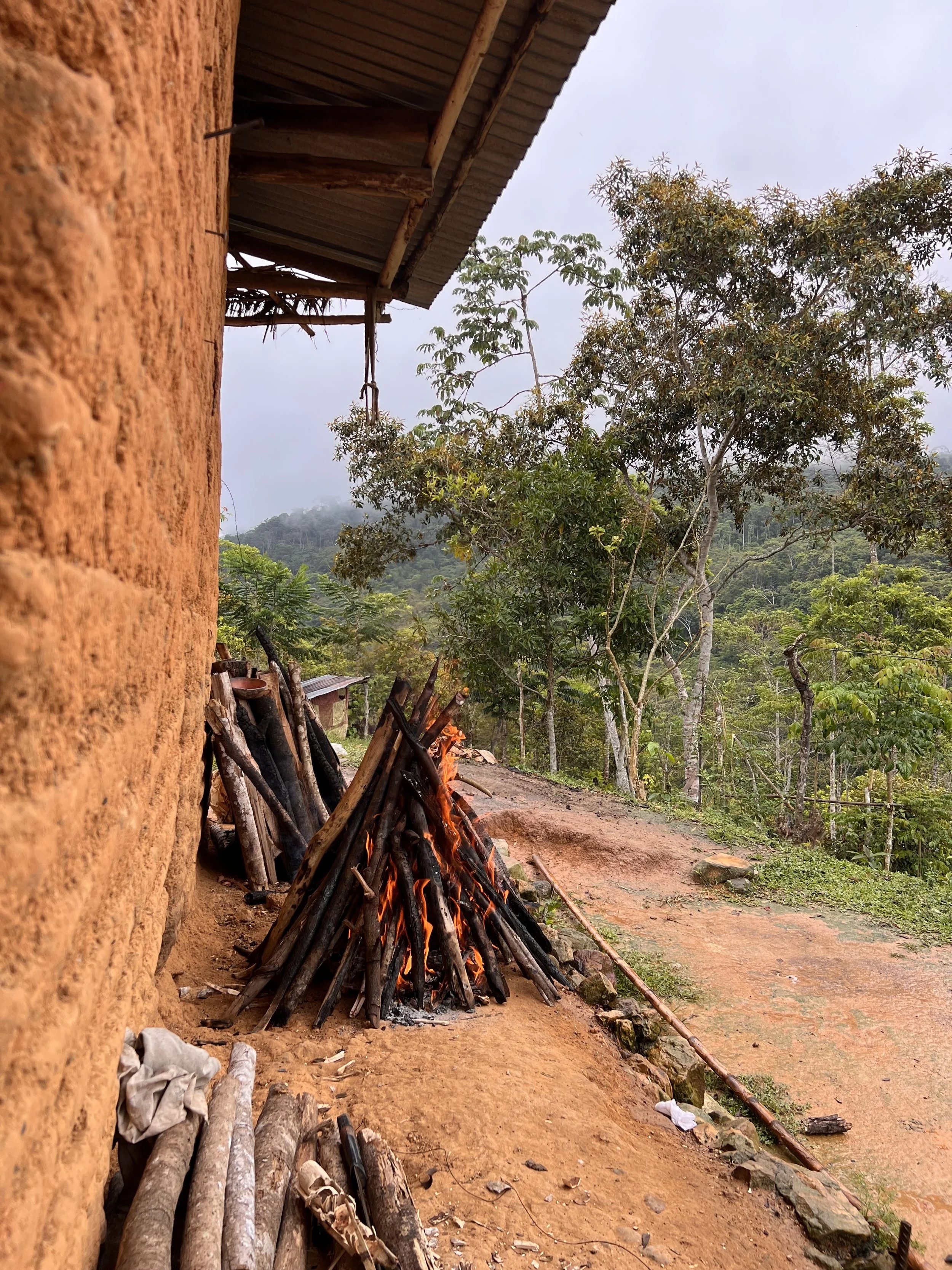 Next to an adobe home, a bonfire blazes with a large piece inside