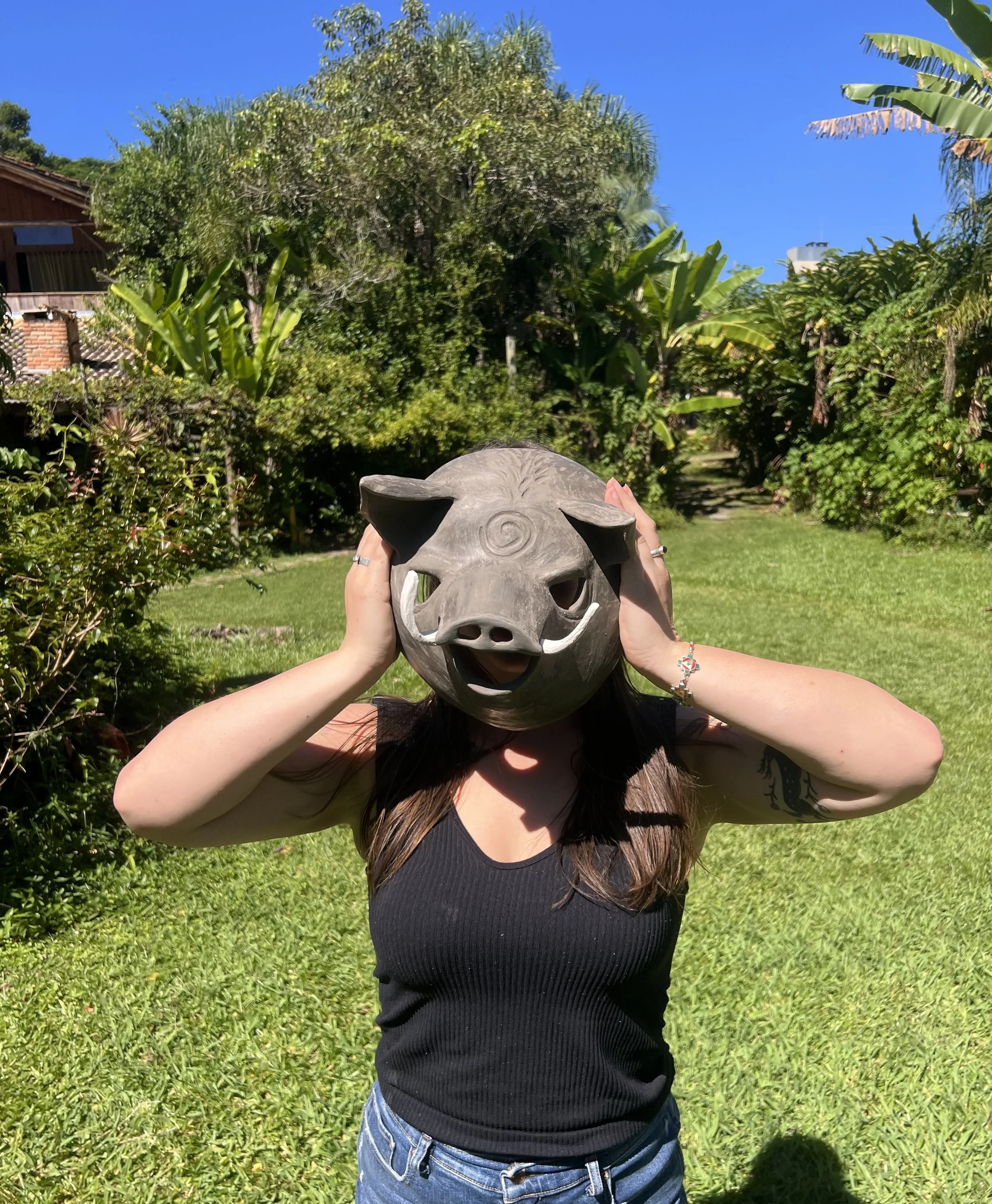 woman holds up a ceramic pig mask to her face