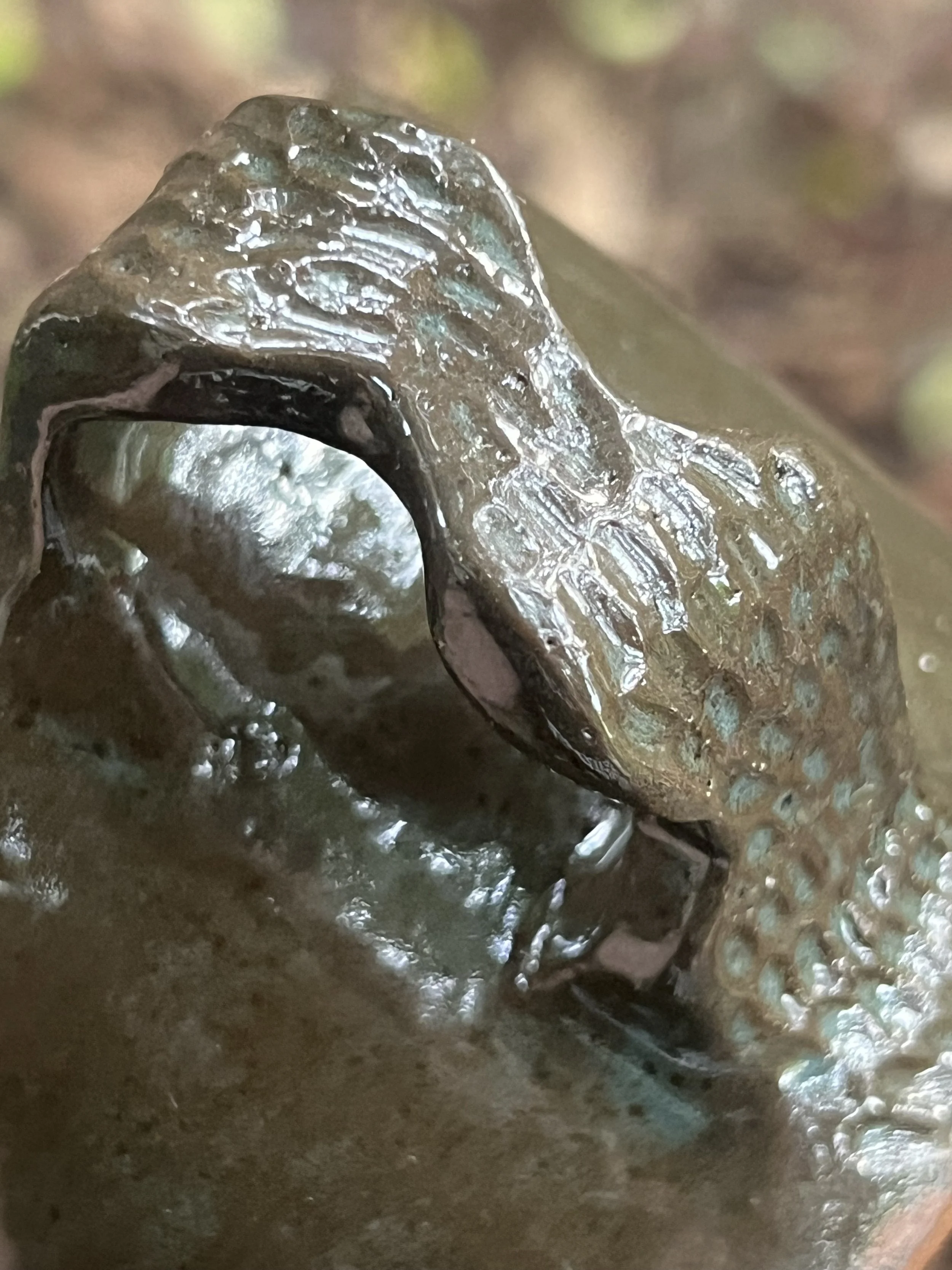 Closeup of a mug handle with a snake pattern carved and dark green glaze