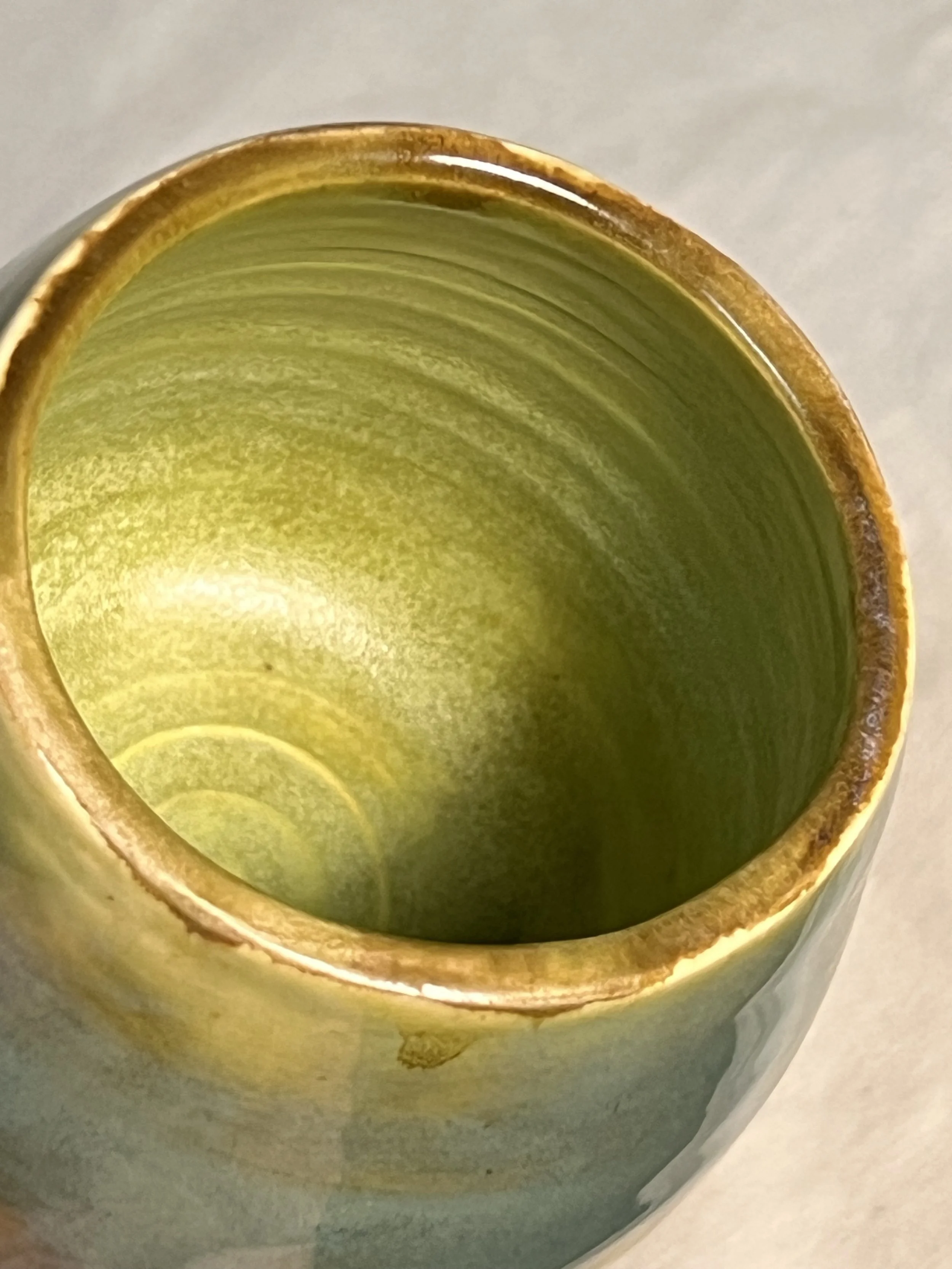Closeup of a high-fired mug with yellow-green inside and glossy teal blue outside.