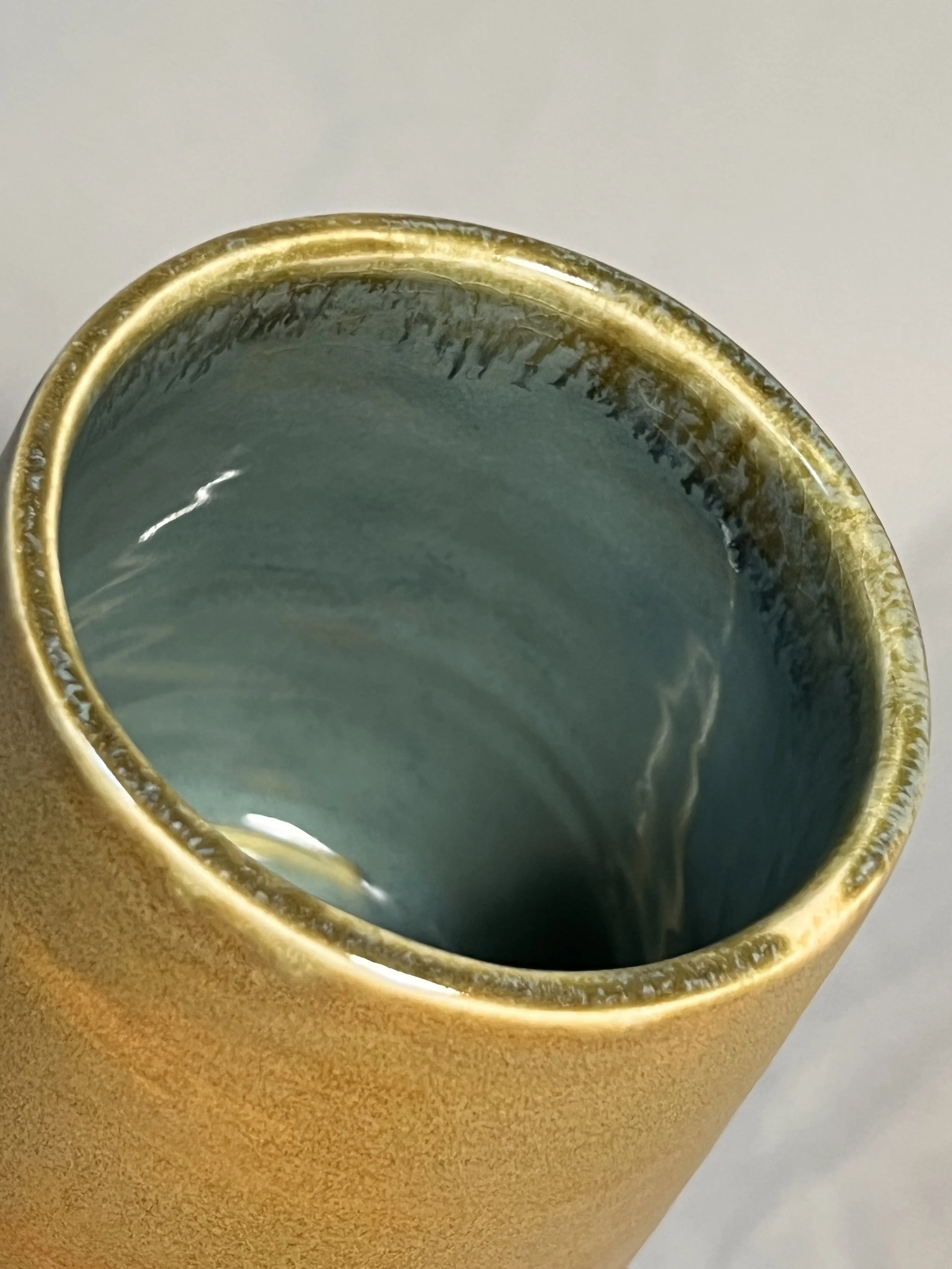 close-up of a mug with a matte yellow glaze on the outside and a glossy blue glaze on the inside