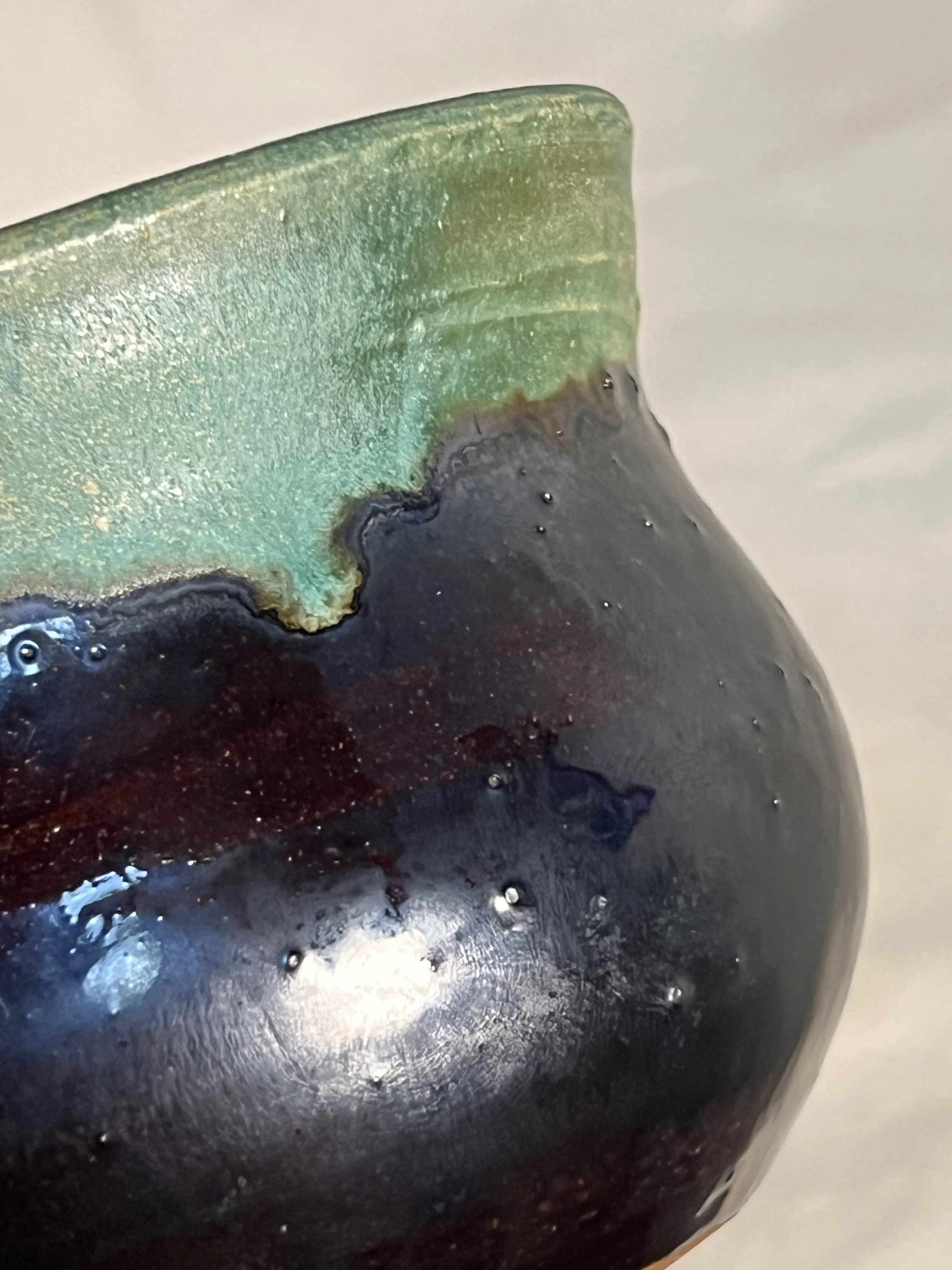 close-up of a vase with shiny black and drippy green glaze