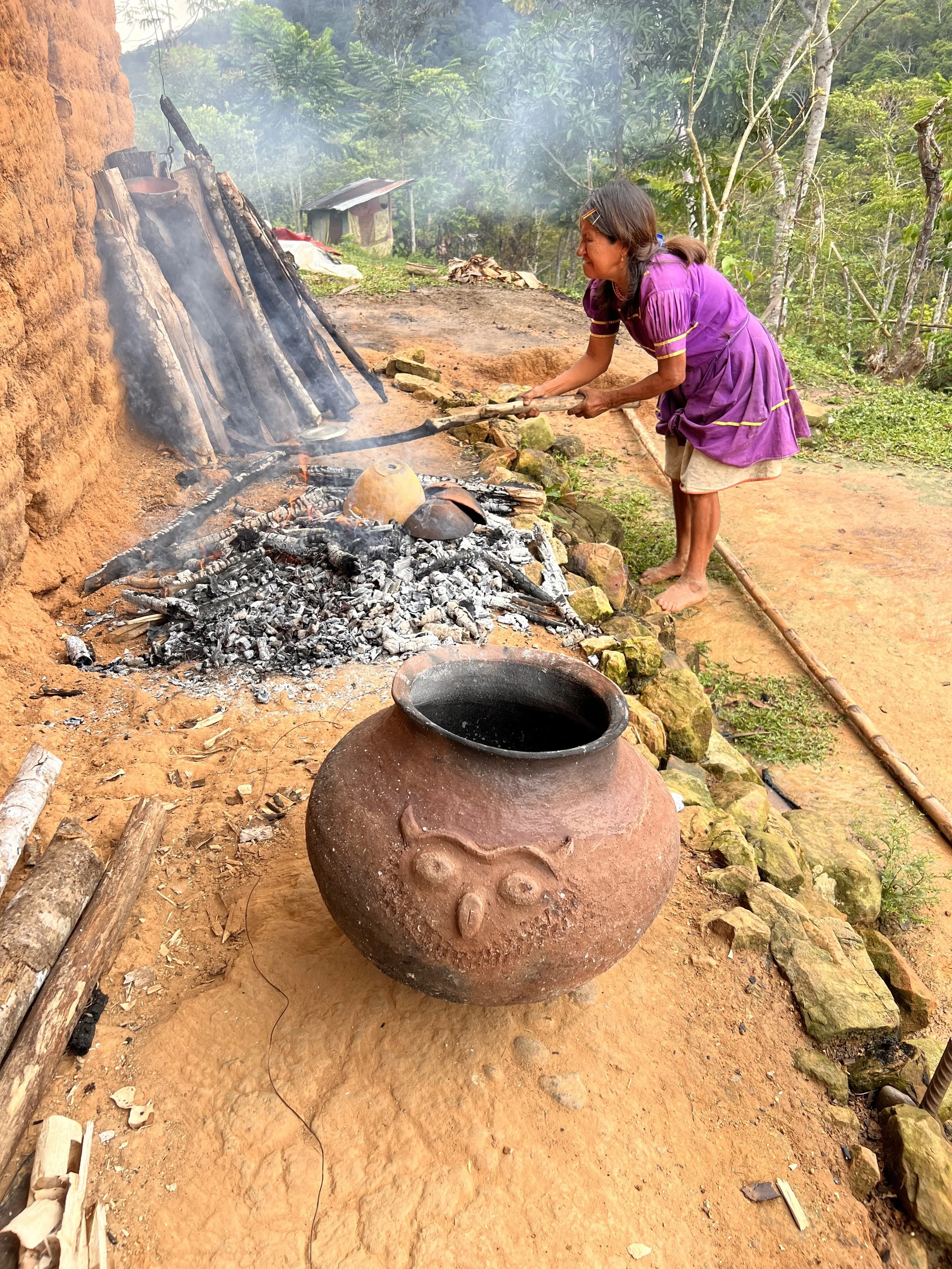 A large pot with an owl face sits next to the ashes of where it was just fired