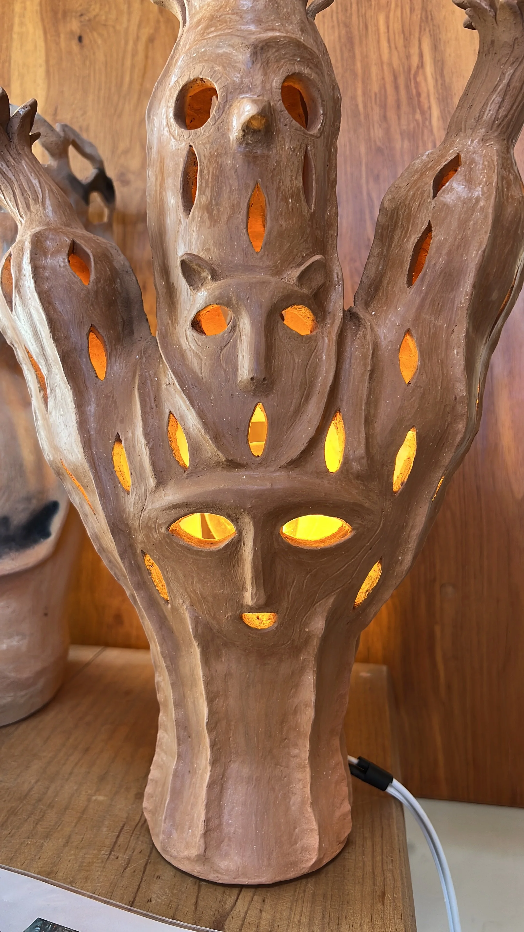 A ceramic or clay lamp with a face design and multiple holes, lit from inside, resting on a wooden surface.