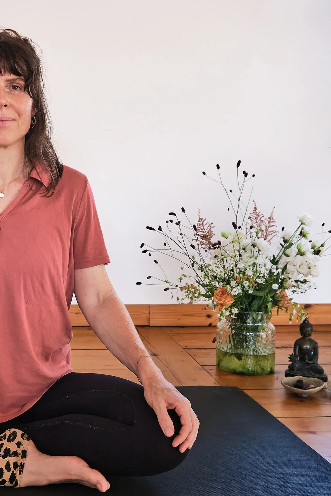 Frau in Yogahaltung, sitzend auf einer Yogamatte neben einem Blumenstrauß in einer Glasvase.