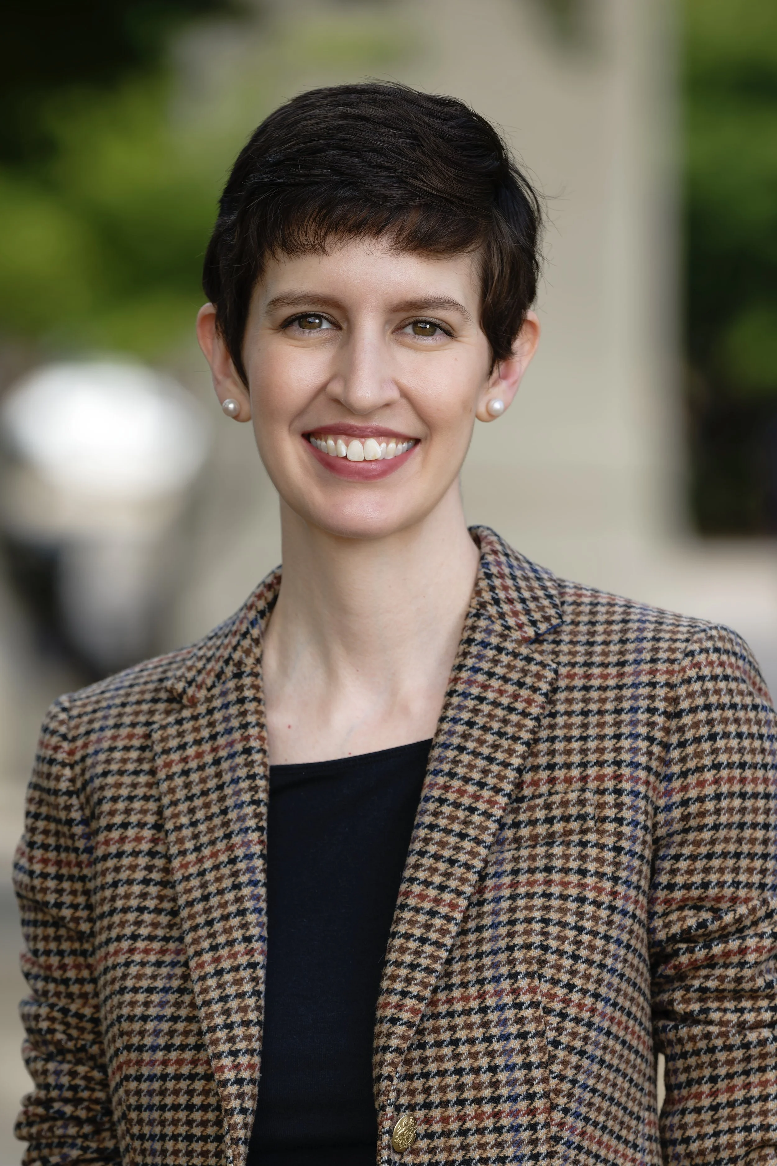 headshot of Emily, a white woman with short dark hair, wearing a plaid blazer