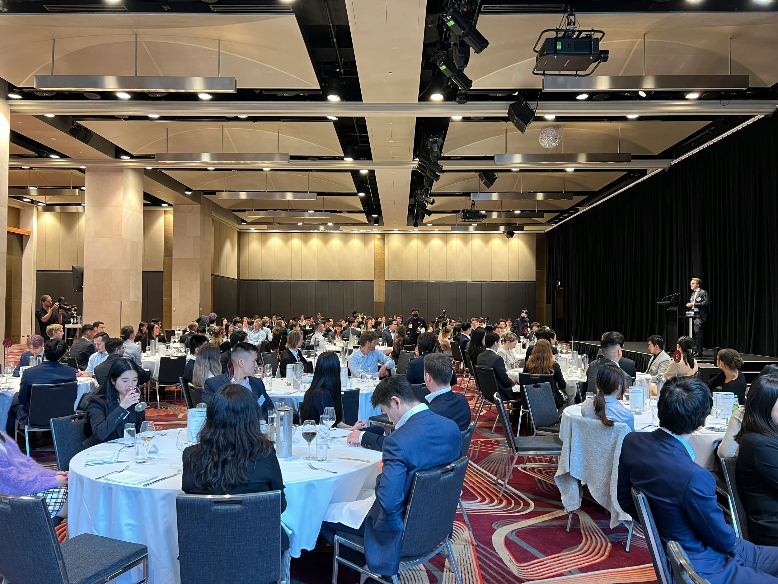 images of round tables full of people attending an event where one man stands on a stage at a podium